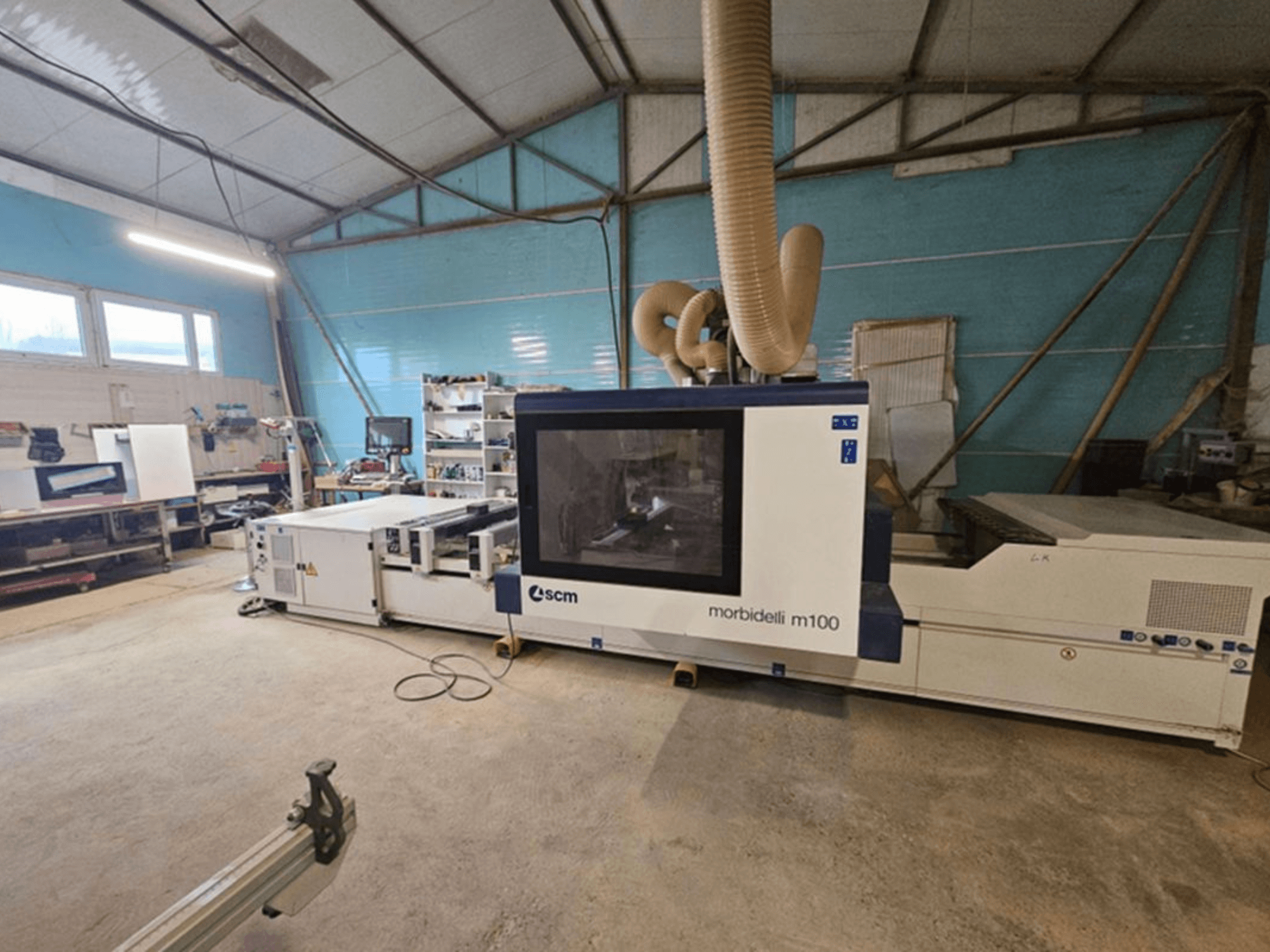 SCM MORBIDELLI M 100 CNC processing center in a workshop, front view with dust extraction and surrounding workspace equipment.