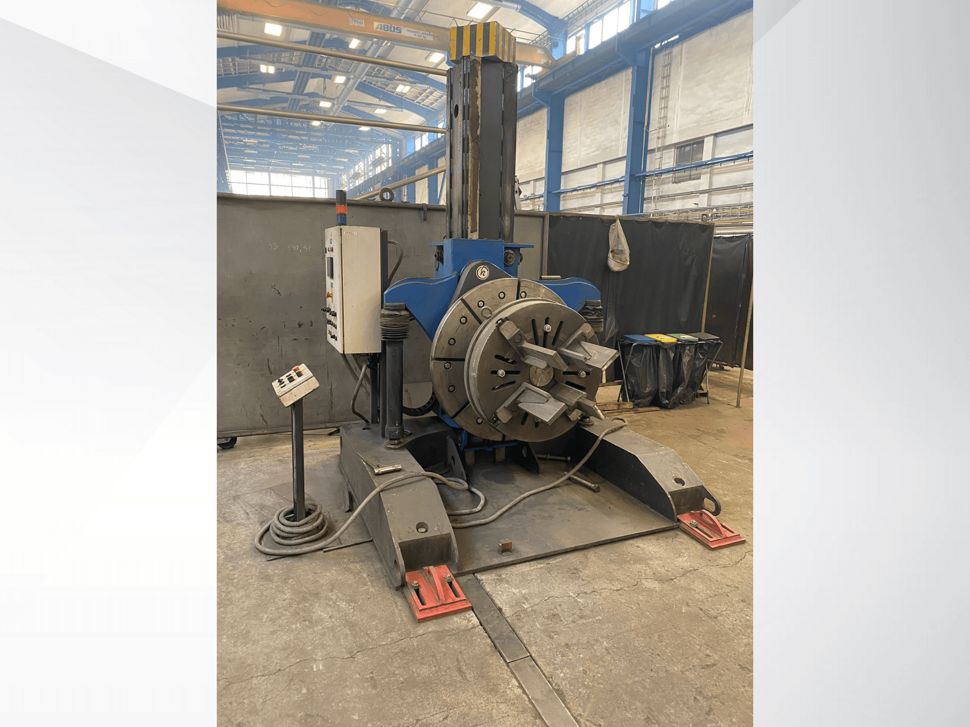 Blue industrial lathe machine with a round rotating head and control panel, side view, in a workshop setting.