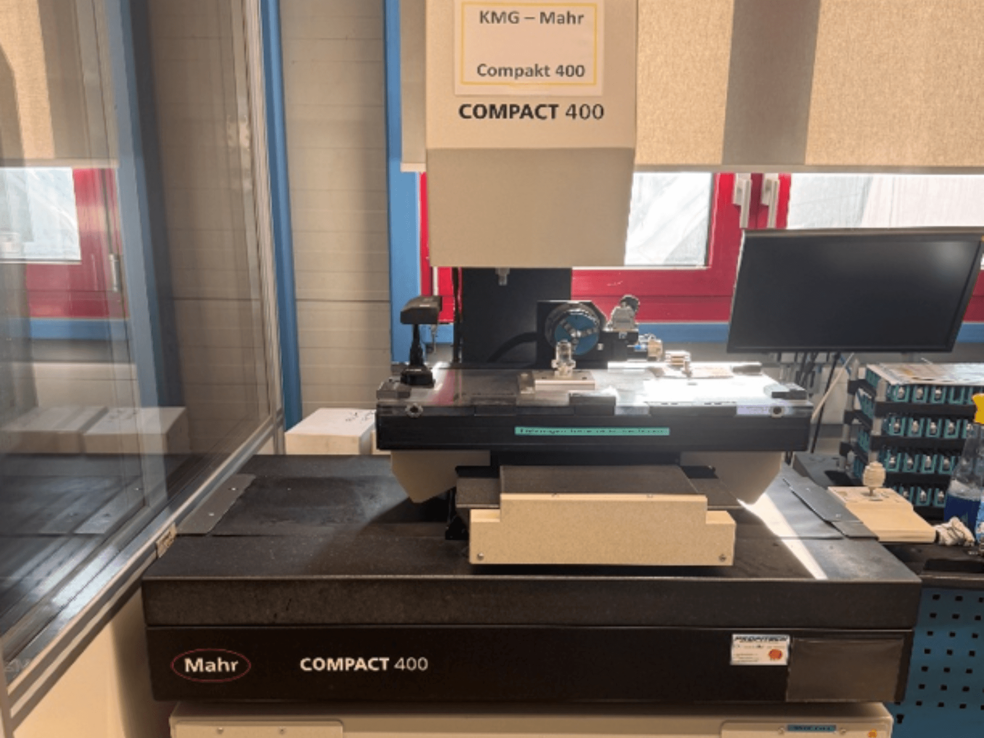 MAHR Compakt 400 Coordinate Measuring Machine shown from a front view, featuring measurement components and a nearby monitor.