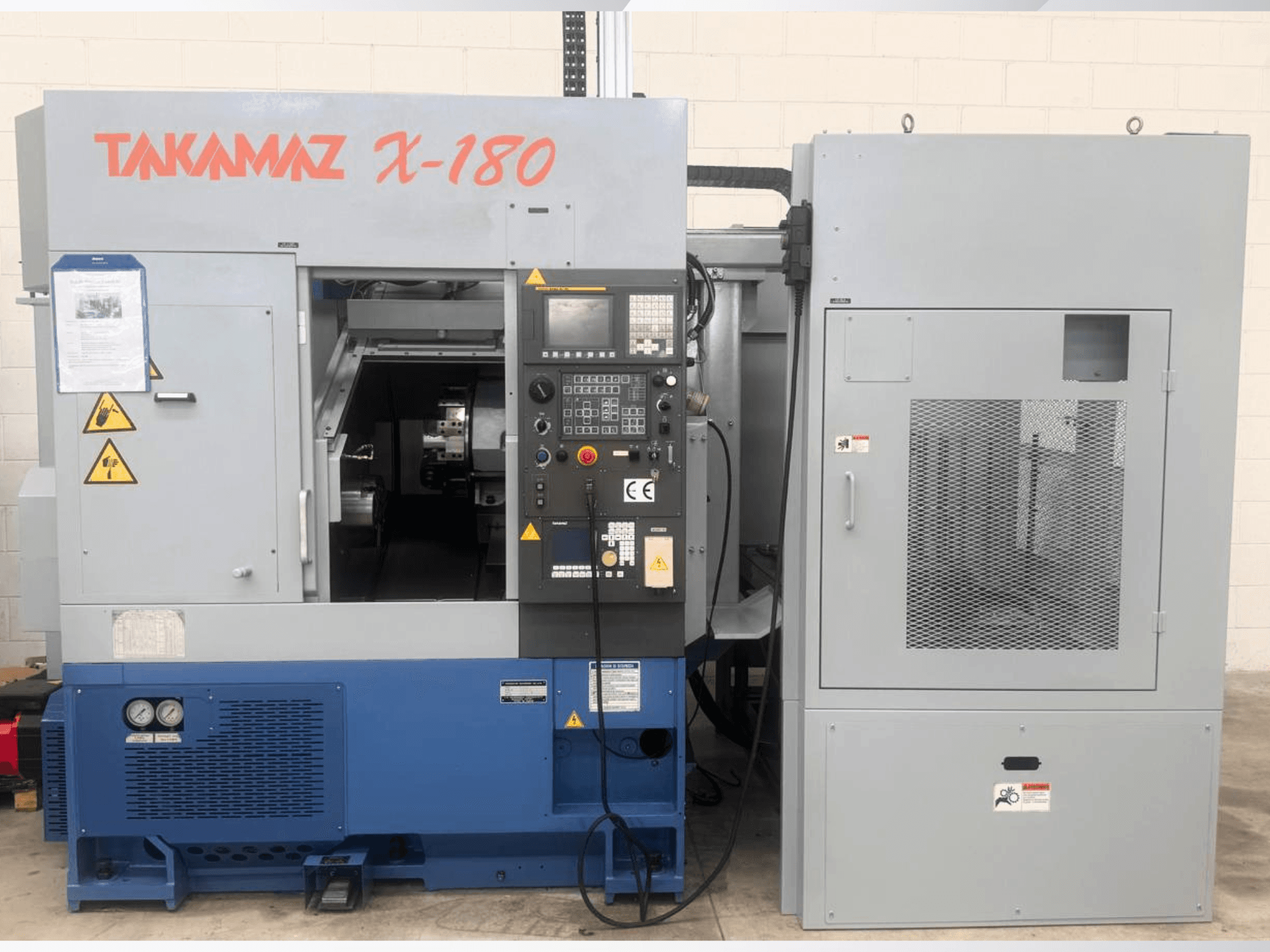 Horizontal turning machine Takamaz X-180, front view showing control panel, safety labels, and adjacent cooling unit.