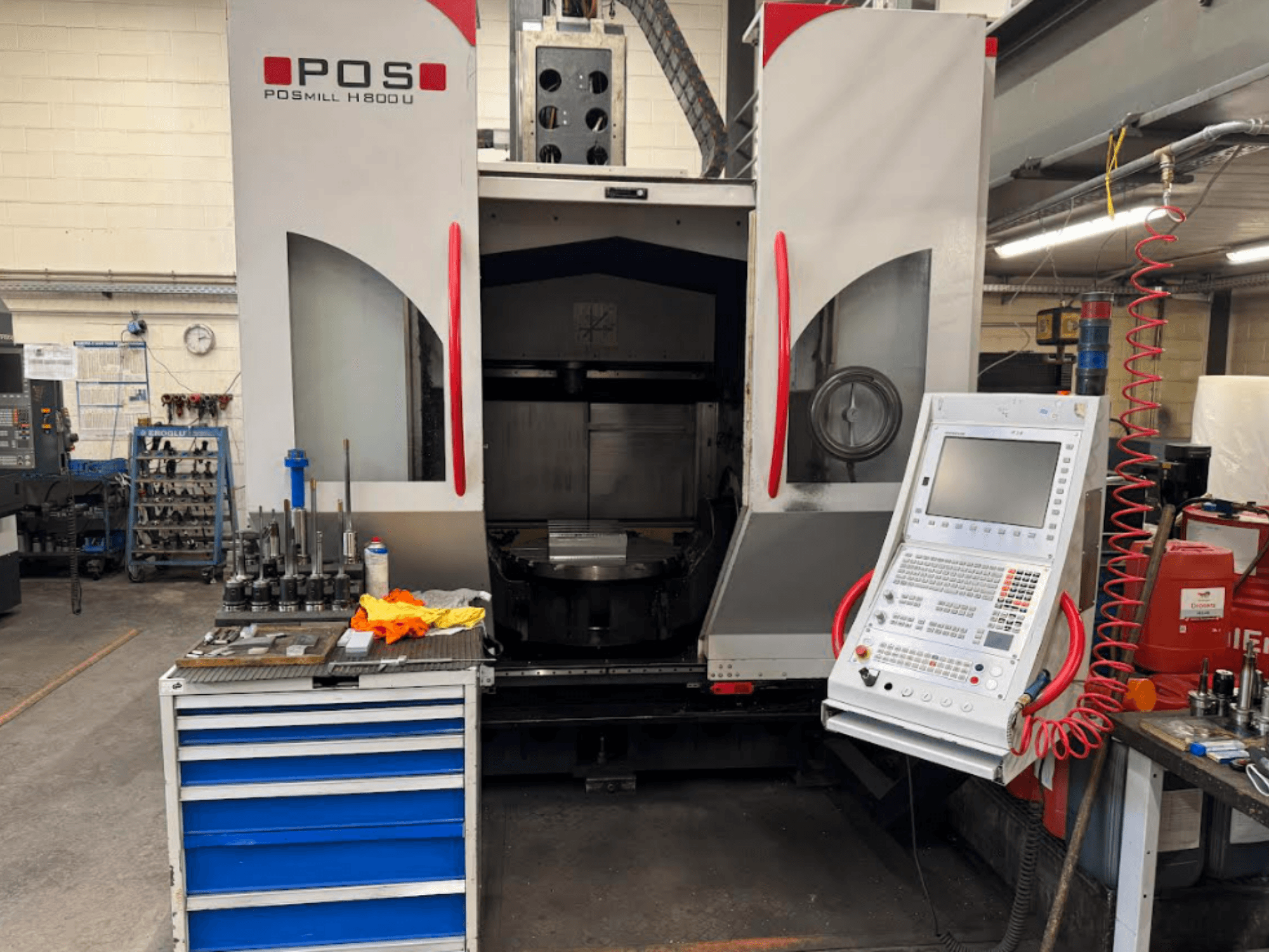 POSMILL H800 U CNC machine viewed from the front, showcasing the control panel and work area with tools and equipment nearby.