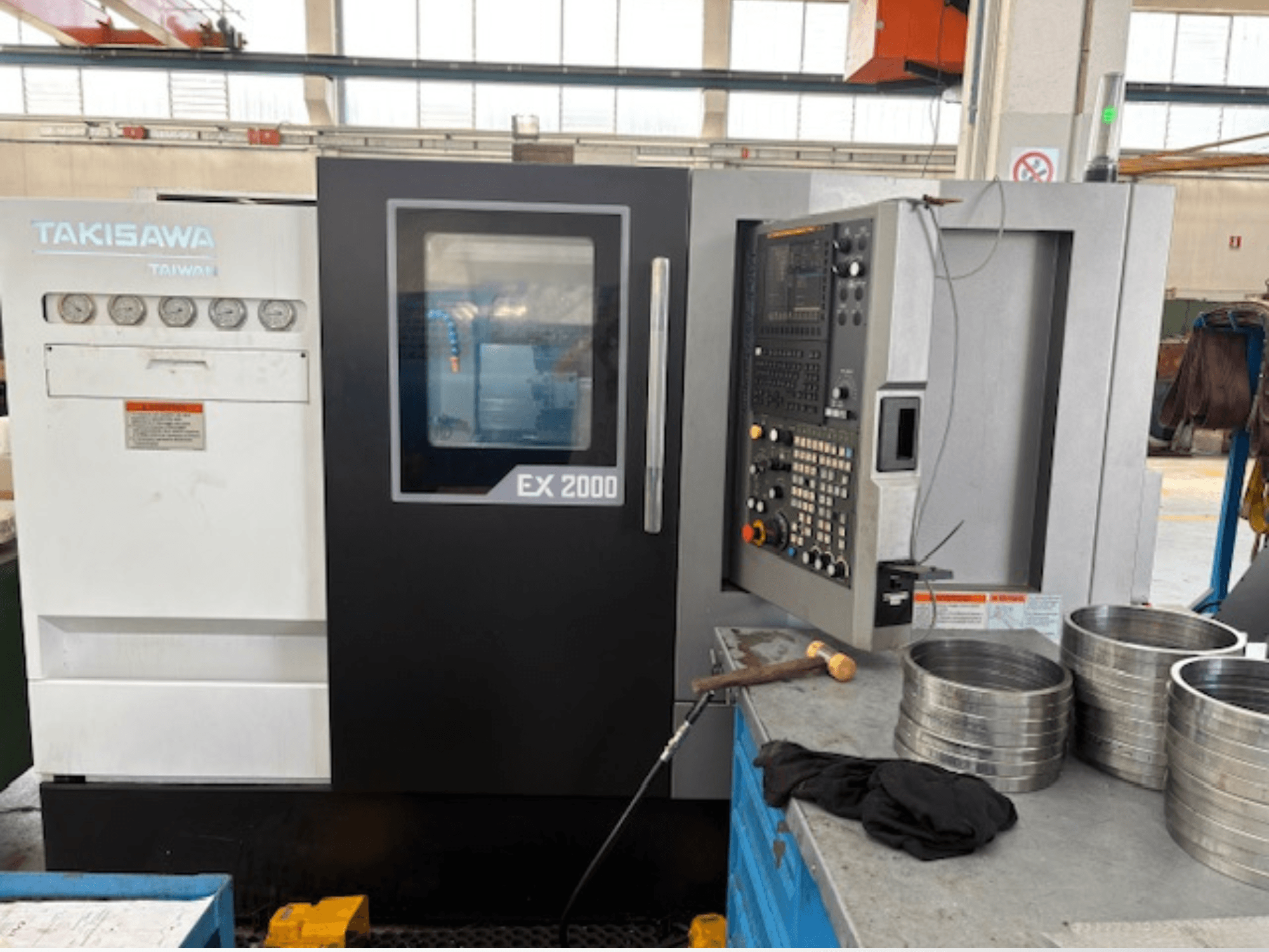 Takisawa EX 2000 CNC machine, front view, featuring control panel, gauges, and metal parts on a workshop table.