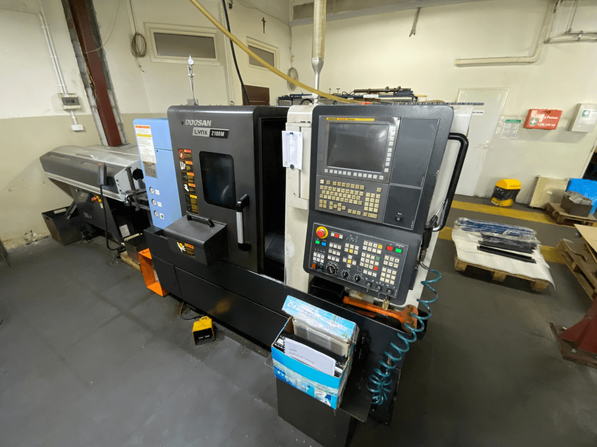 DOOSAN LYNX 2100MA horizontal turning machine seen from a side view, featuring control panel, tools, and work area.