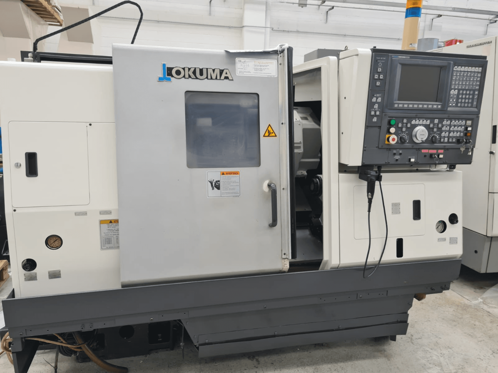 Okuma LB 300M X 500 horizontal turning machine in side view, showcasing control panel, spindle access, and safety warnings.