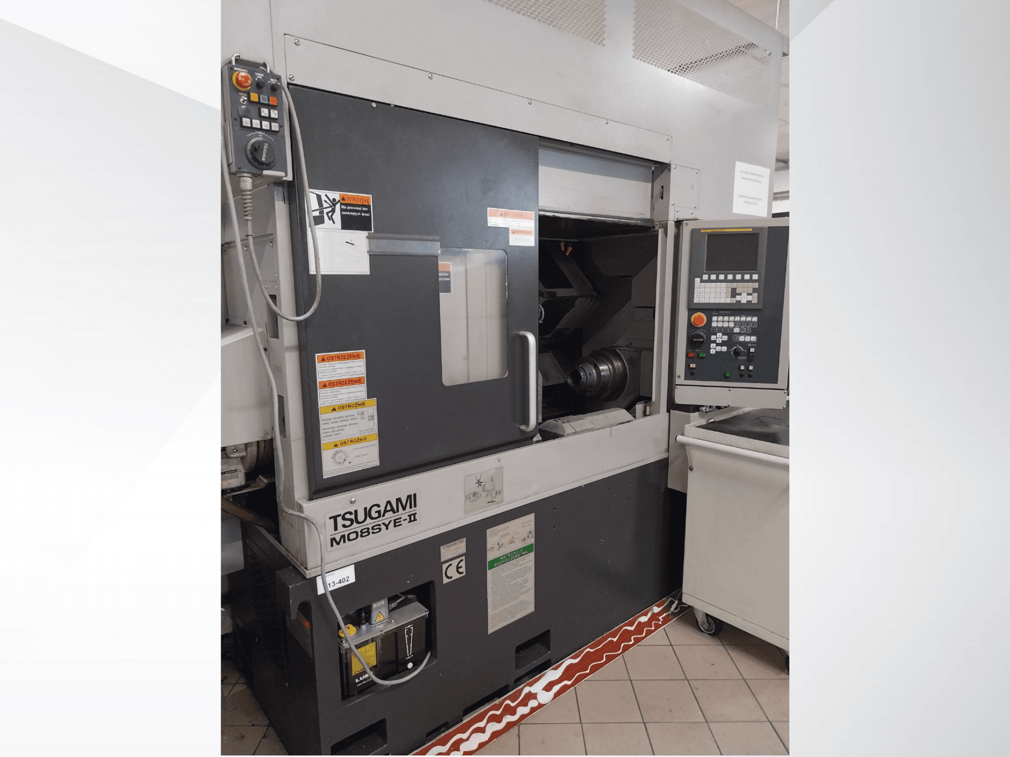 Tsugami M08SY-II CNC lathe, front view, showing control panel, spindle, and loading area. Features safety notices and brand label.