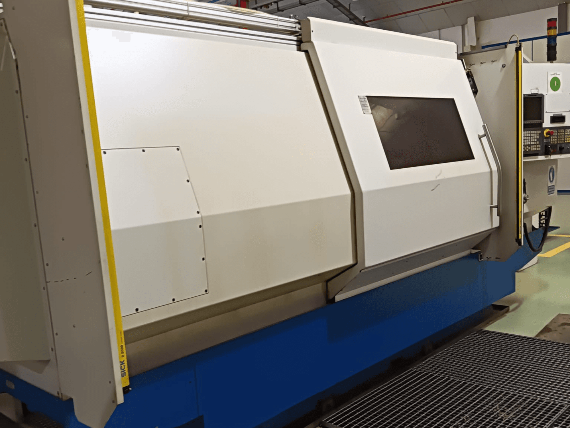 Industrial lathe machine, side view, featuring a large white and blue casing, digital control panel, and safety features.