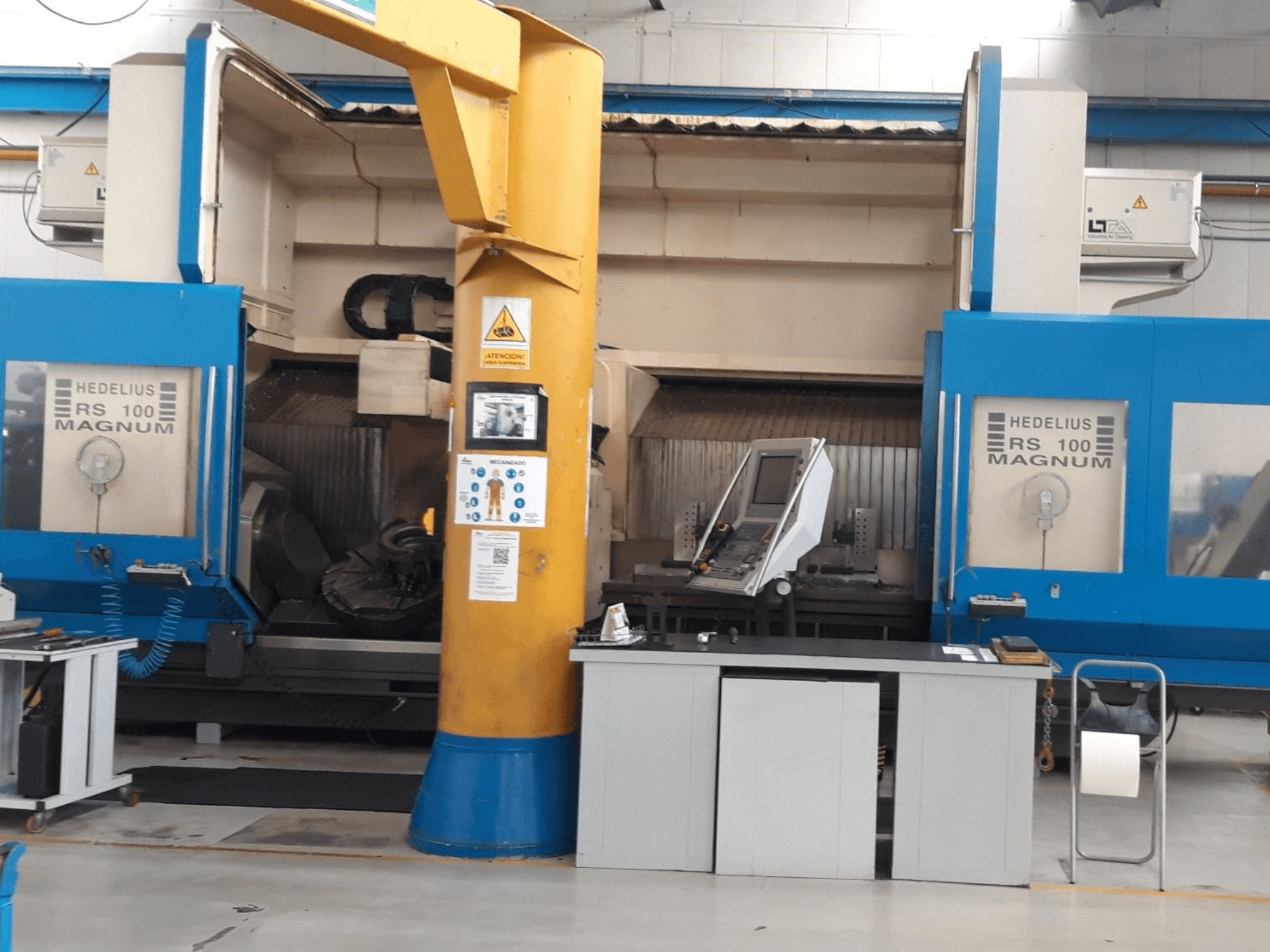 HEDALIUS RS 100 MAGNUM machine, front view; features control panel and yellow support column, set in an industrial workspace.
