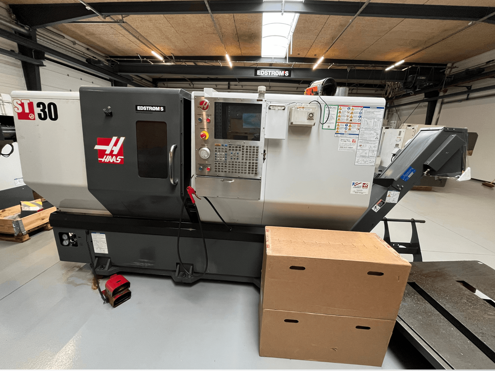 Haas ST-30 CNC lathe viewed from the side, featuring a control panel, model badge, and two cardboard boxes nearby.