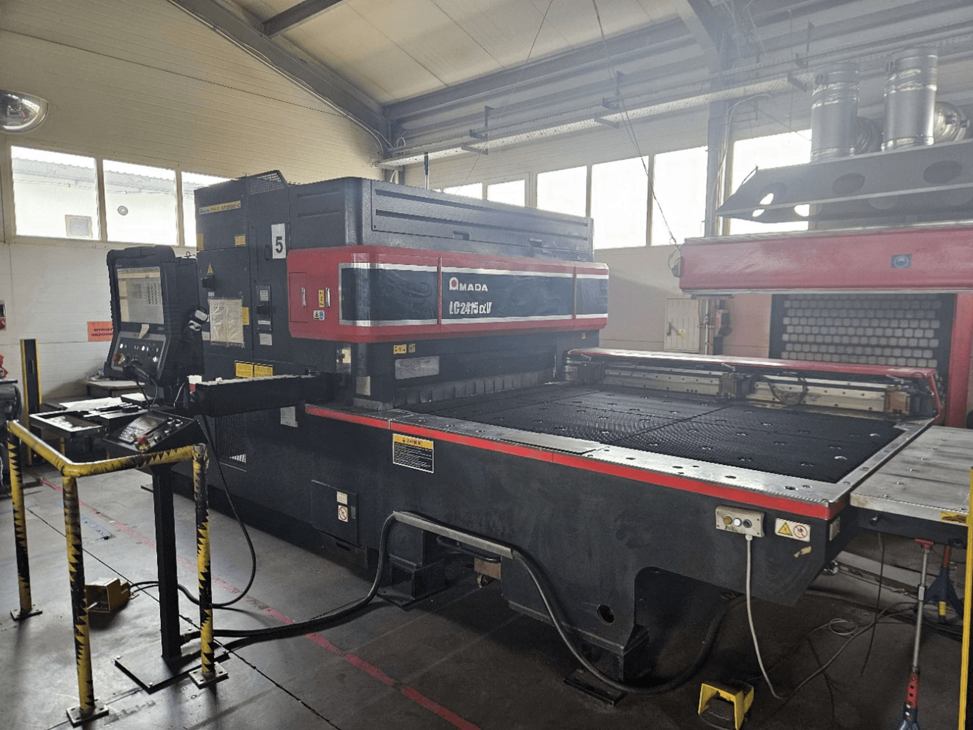 AMADA LC2415 Alpha 5 CO2 laser cutting machine, front view showing control panel and cutting bed with safety barriers.