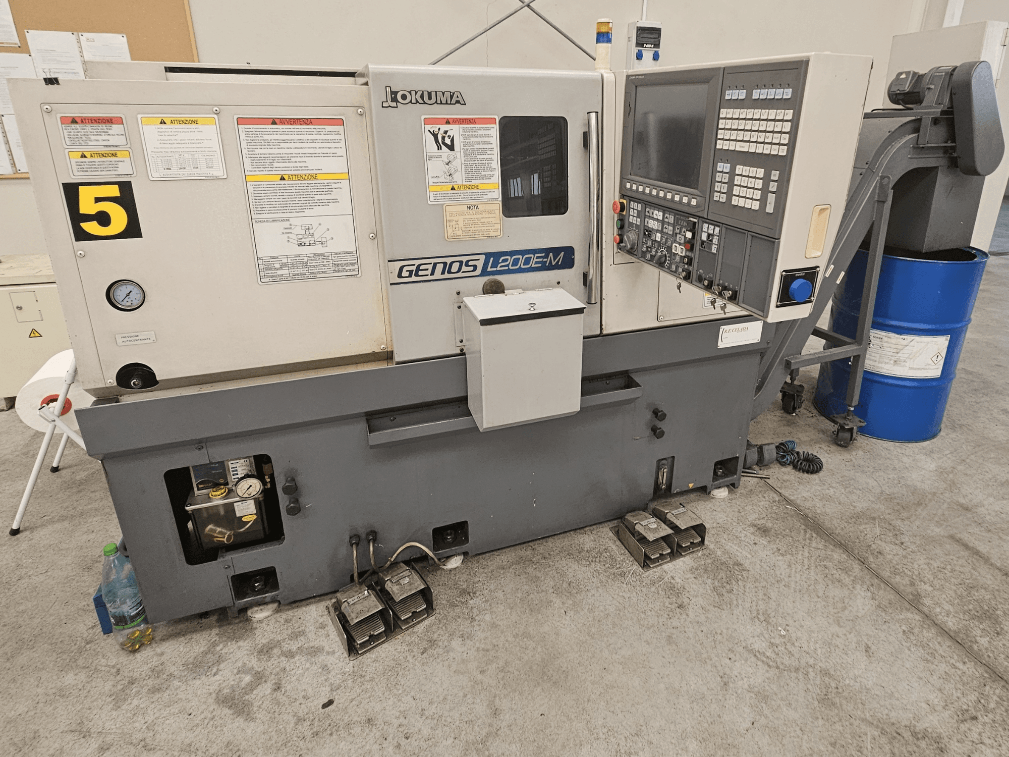 Okuma GENOS L200E-M horizontal turning machine in front view, featuring control panel, labels, and coolant barrel.