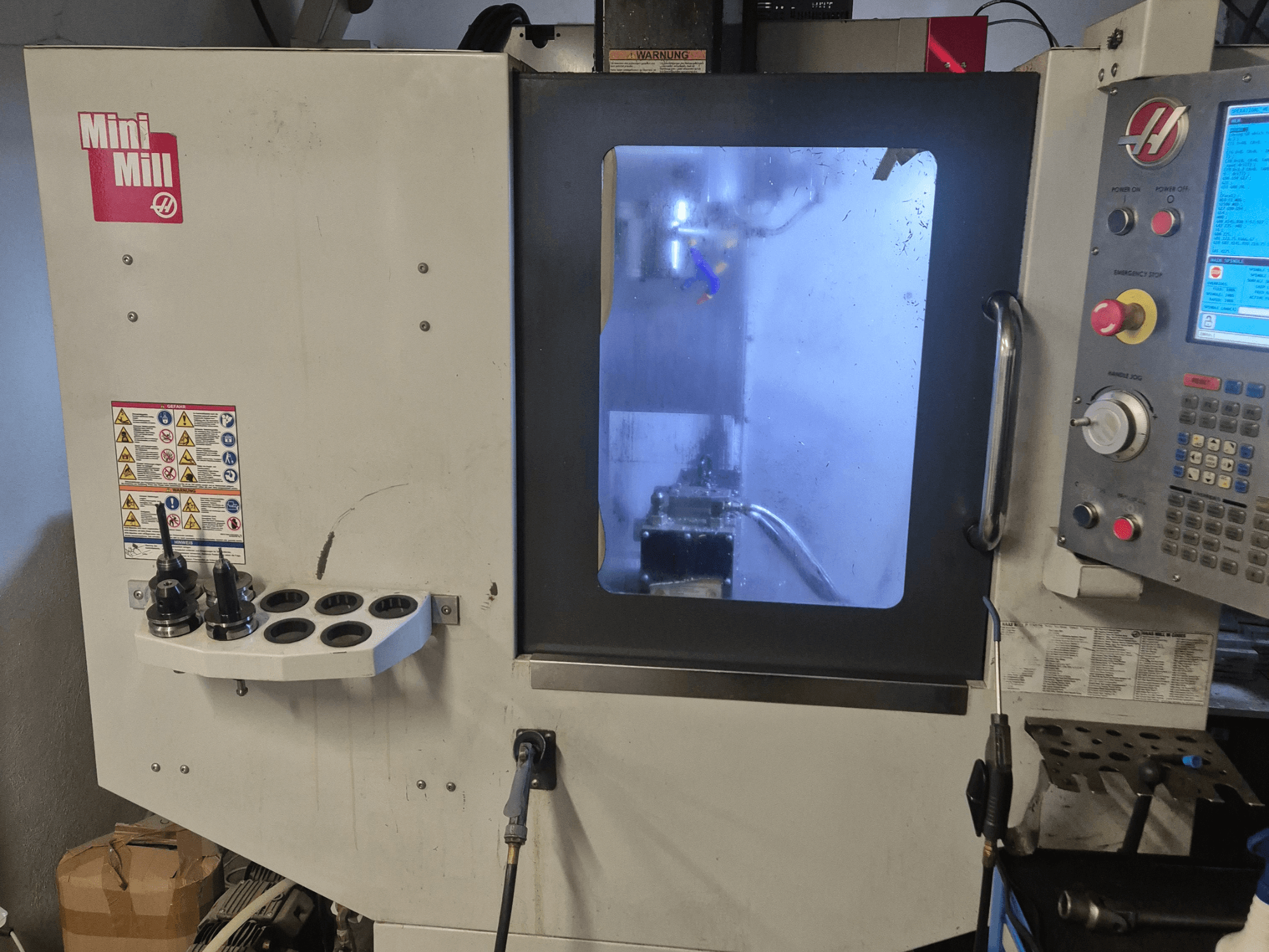 Front view of HAAS Mini Mill, showcasing control panel, tool holders, and view into machining area with coolant.