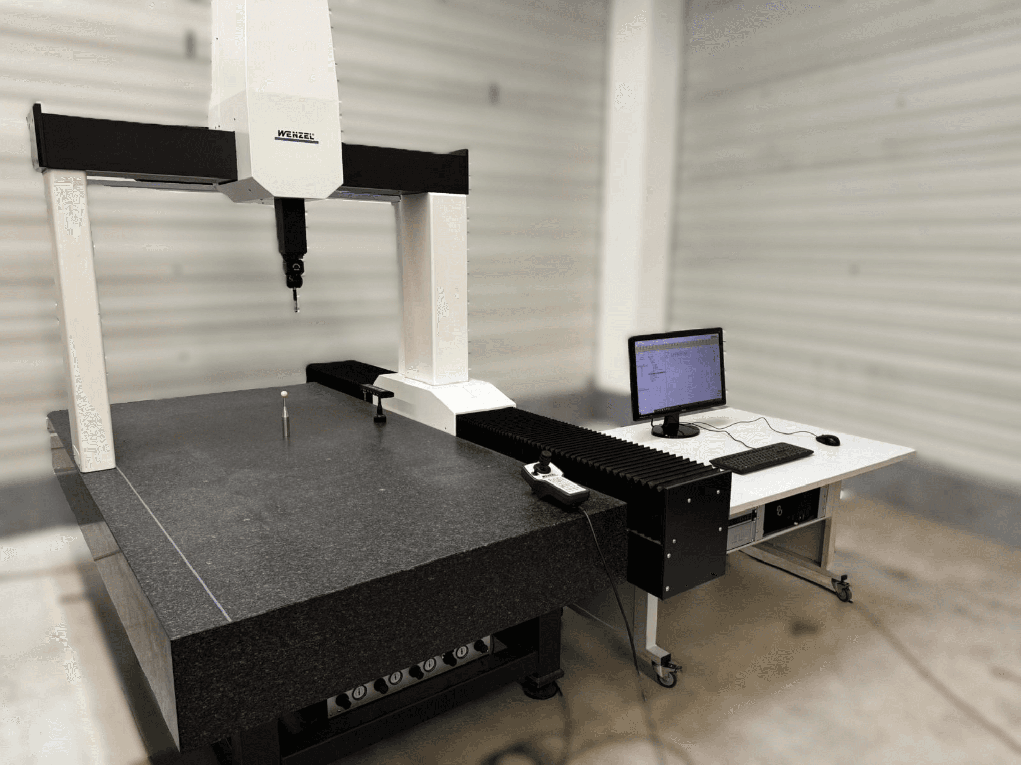 Wenzel XO 87 CMM in a front view, featuring a measurement probe and a granite table with a computer setup beside it.