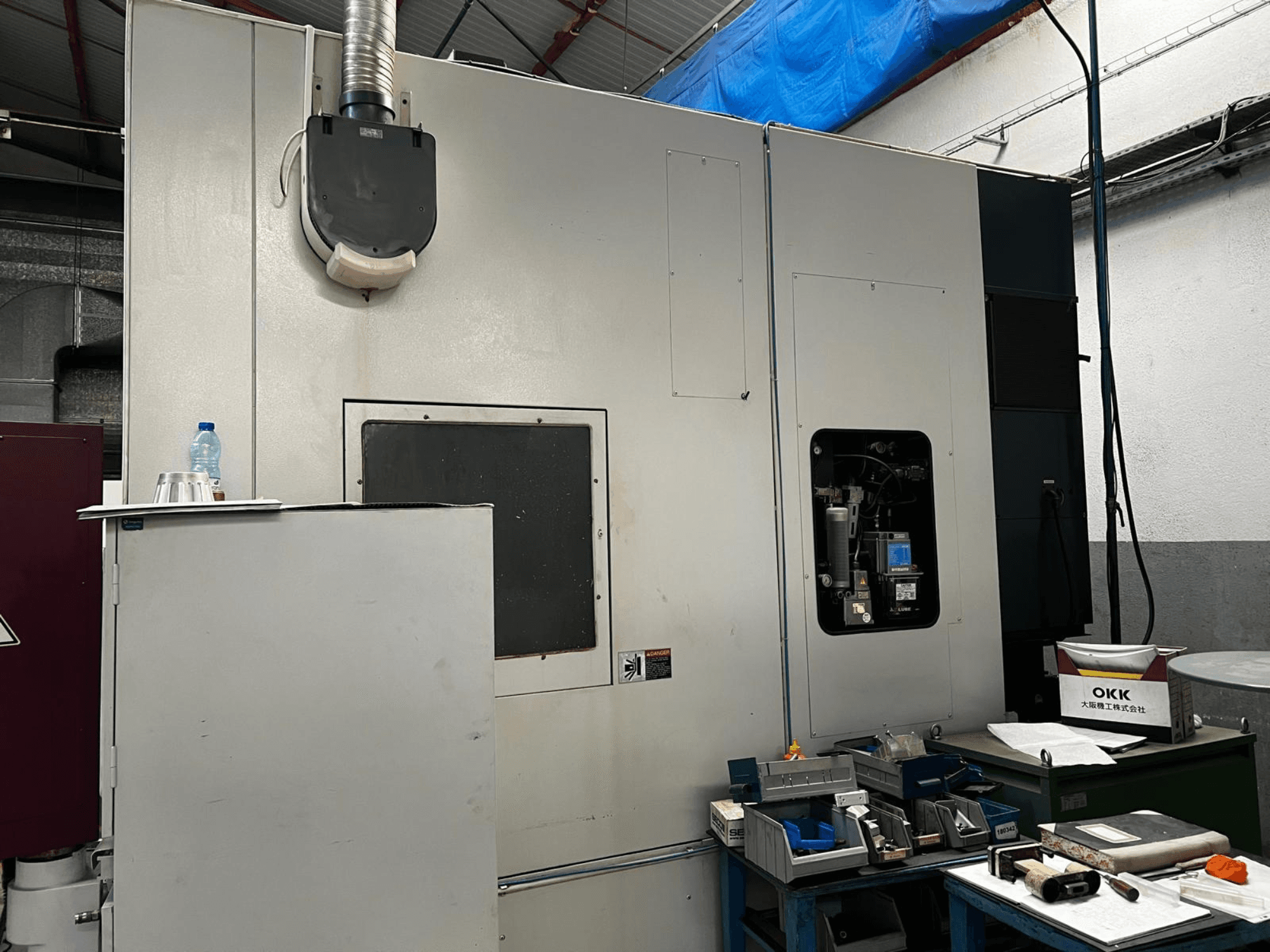 OKK VP600 Vertical Machining Centre in a workshop, side view showing machine details and tools on a nearby table.
