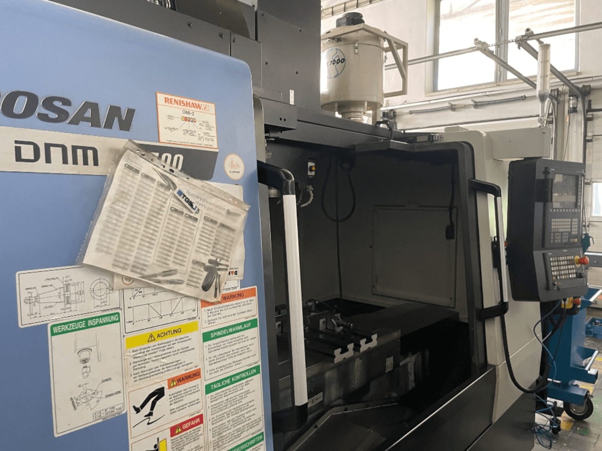 DOOSAN DNM 5700 vertical machining center, front view, shows control panel, safety labels, and machine details.