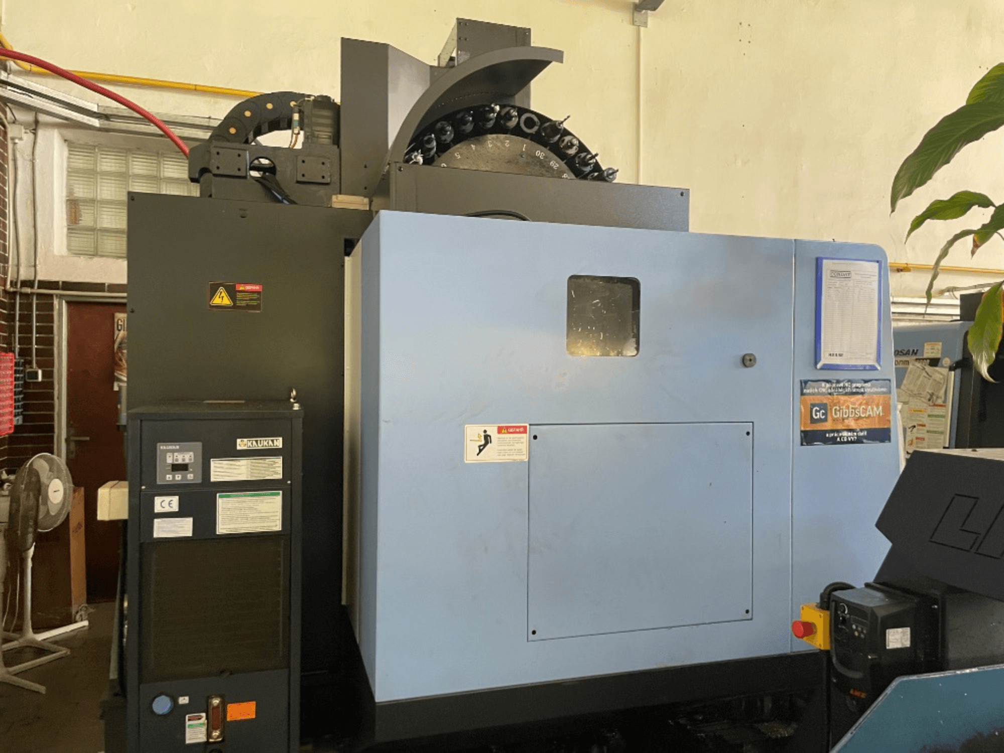 Front view of a DOOSAN DNM 5700 vertical machining centre, showing control panel, safety labels, and machine features.