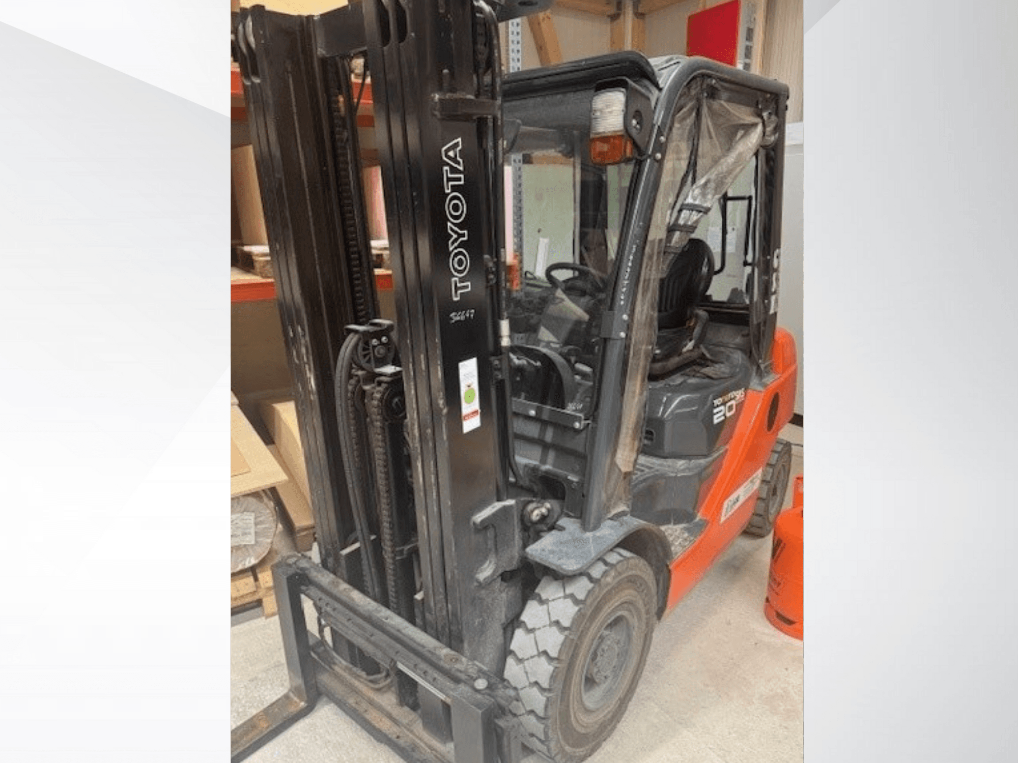 Toyota 20 forklift viewed from the front, featuring a black mast, transparent cabin, and orange propane tank beside it.