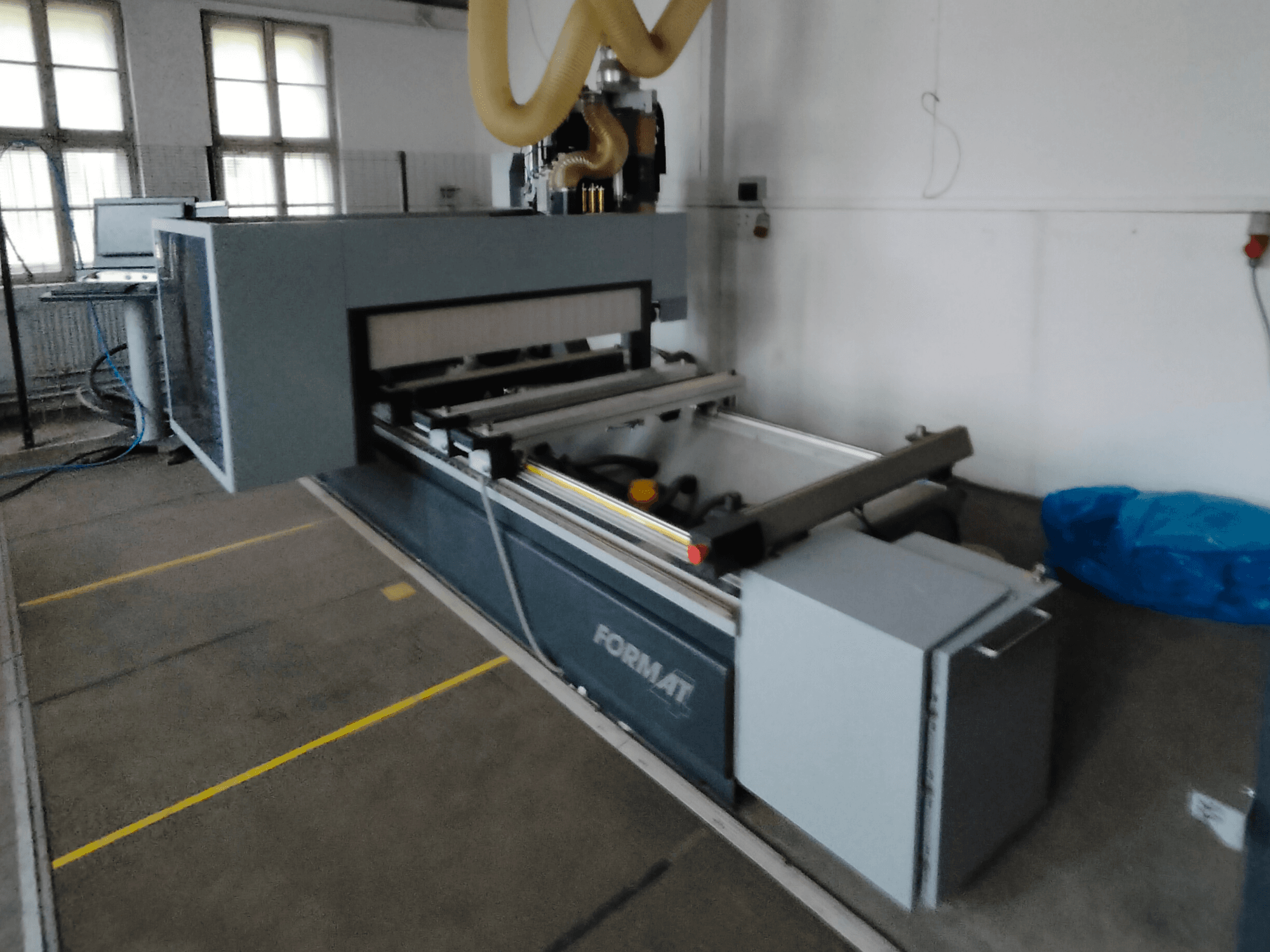 Front view of a Format CNC machine with a gray body, featuring guide rails and a visible control panel.