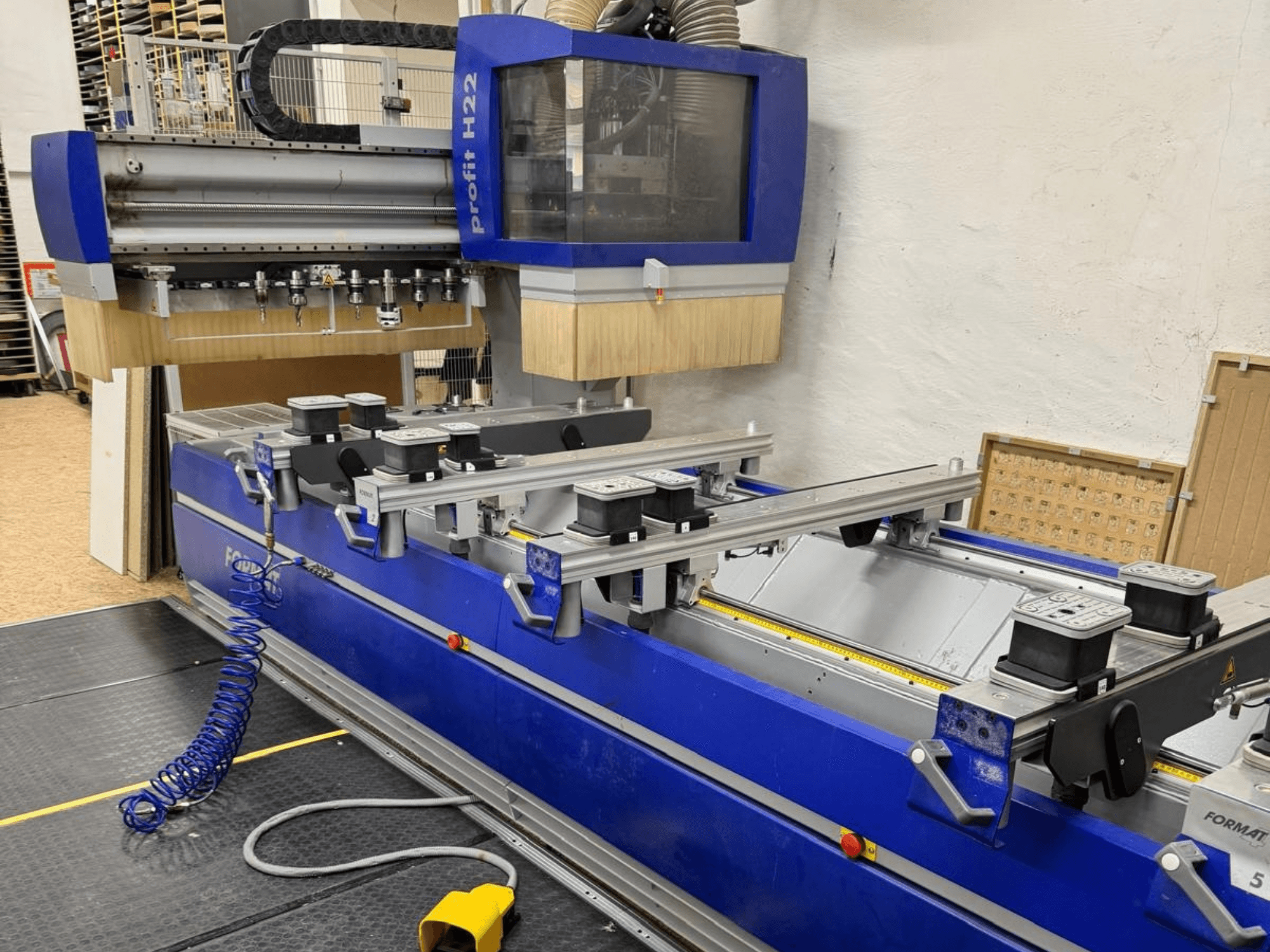 FORMAT4 PROFIT H22 CNC wood machining center, front view, with machining tools and holding clamps visible on blue body.