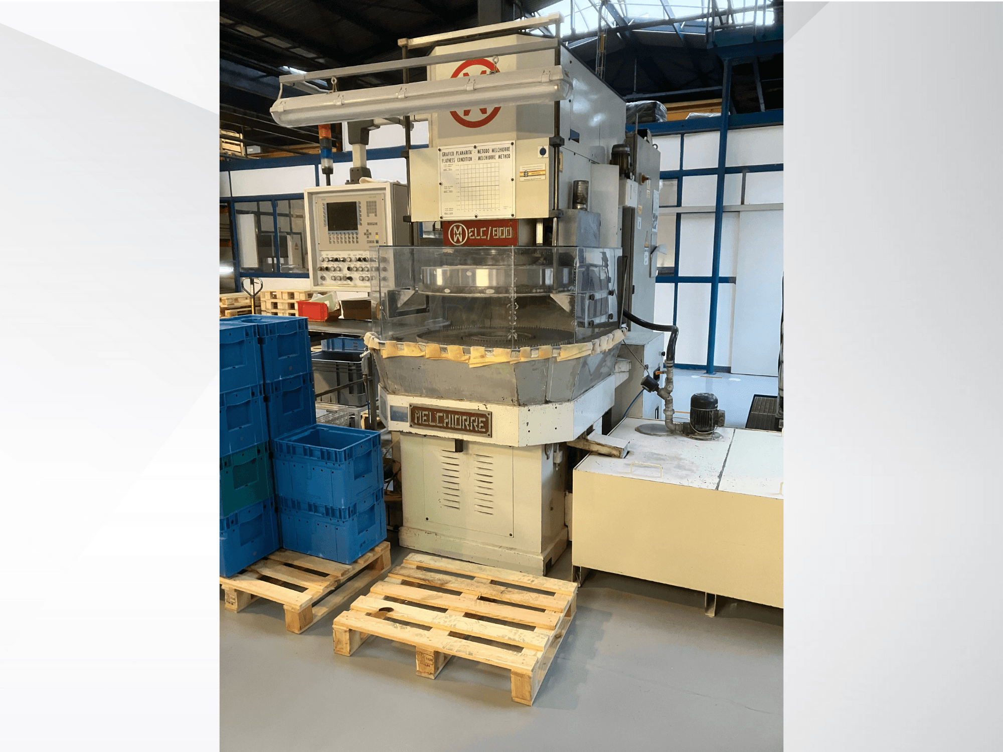 Melchiorre industrial machine at front view, featuring control panel, clear hopper, and blue crates on wooden pallets.