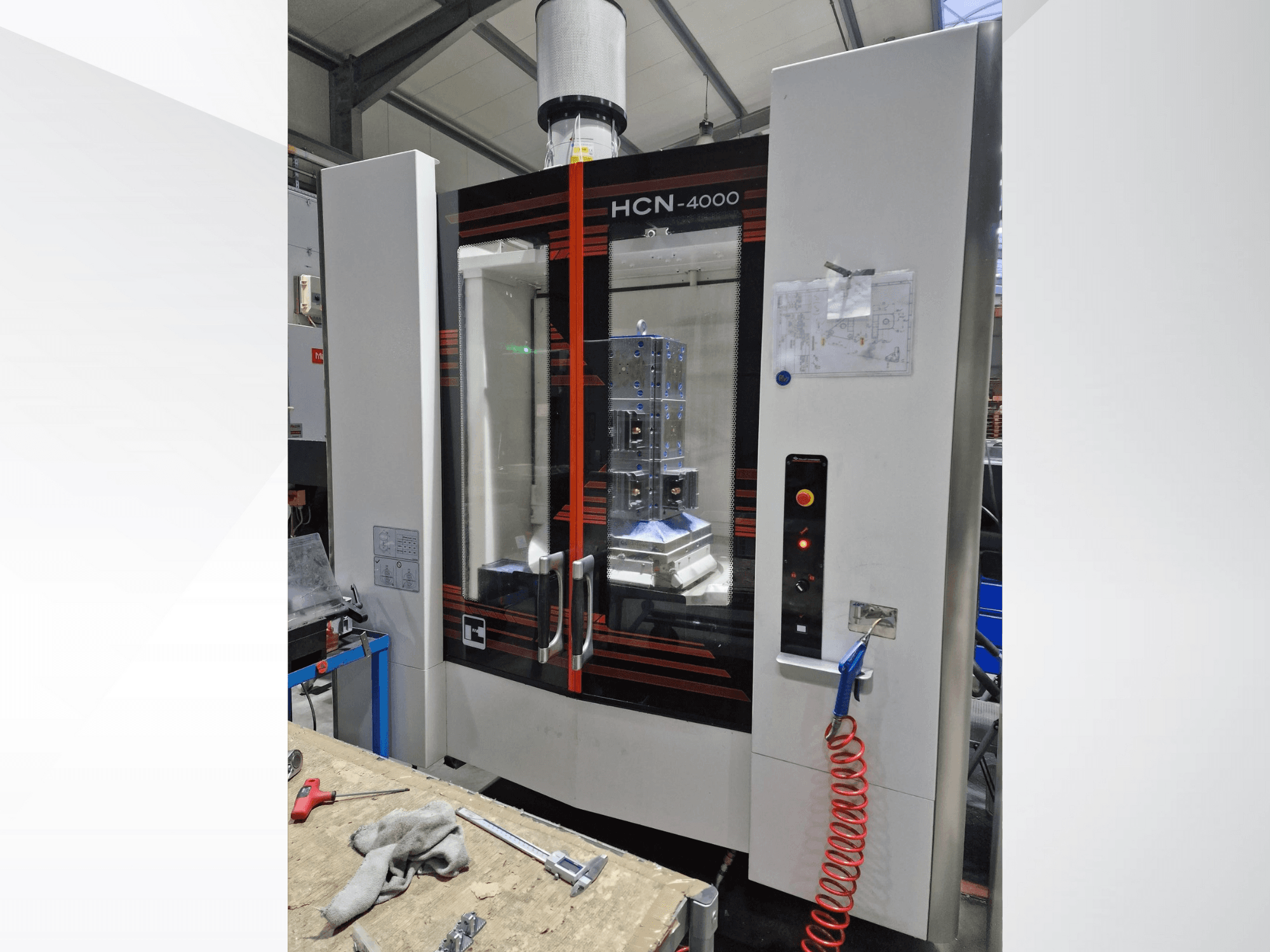 HCN-4000 CNC machine in front view, featuring a glass panel, control panel with buttons, and a blueprint attached.