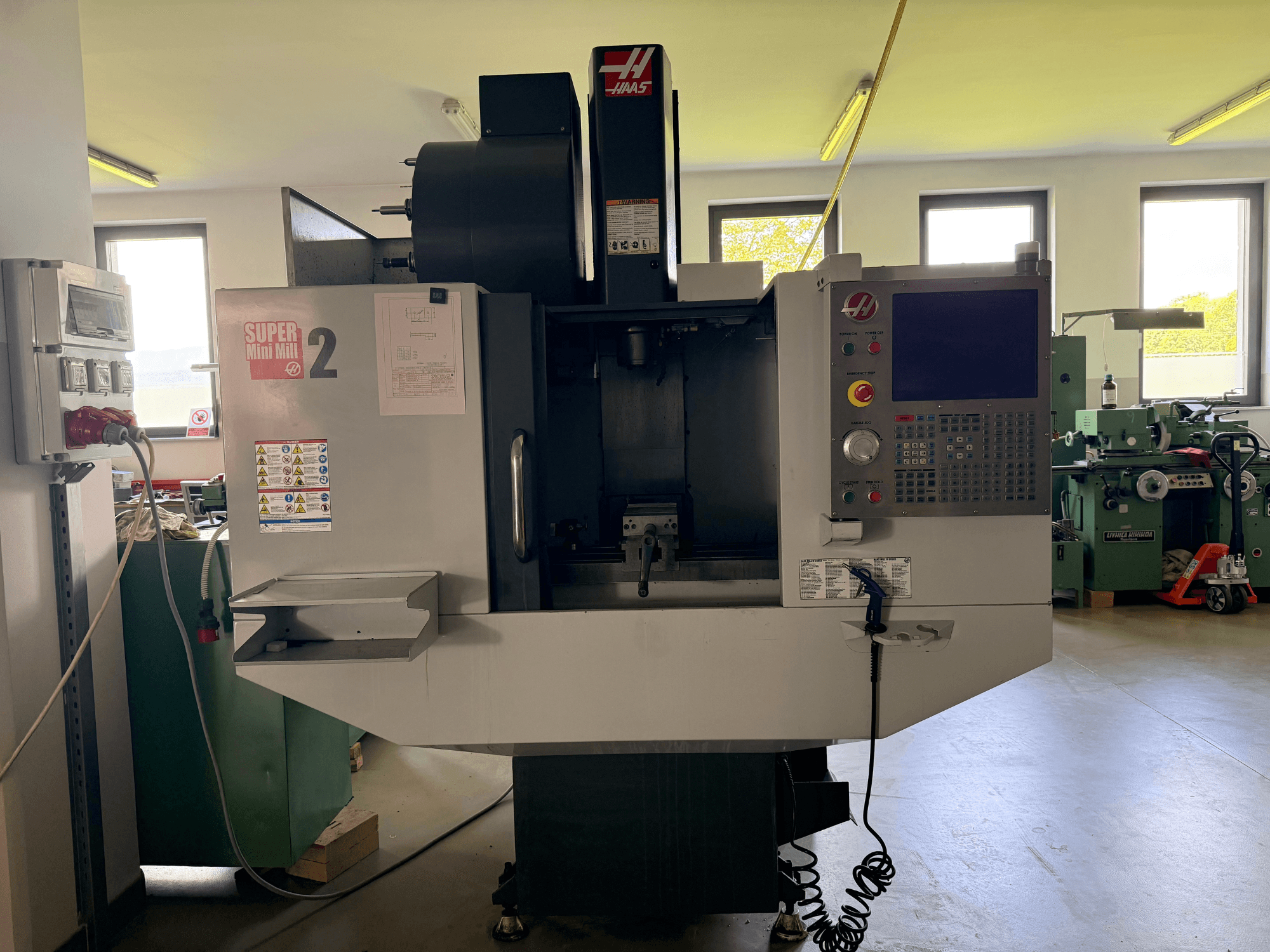 Haas Mini Mill 2 vertical machining center in front view, showcasing control panel and tool area with warning labels.