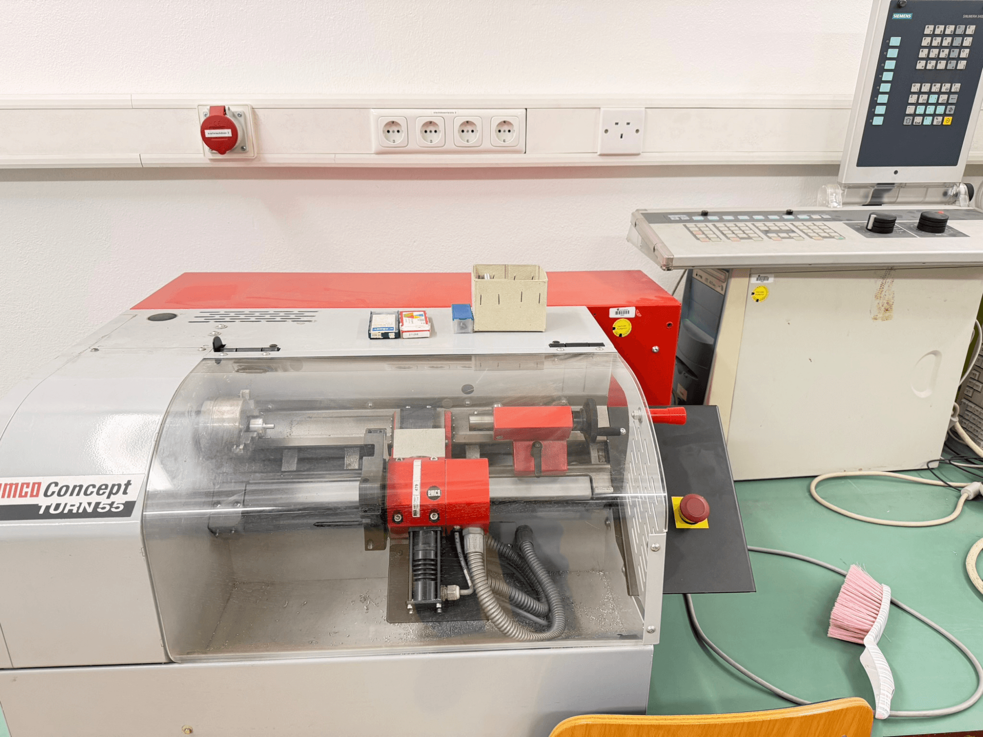 EMCO Concept Turn 55 horizontal turning machine with red and gray exterior, front view showing controls and work area.