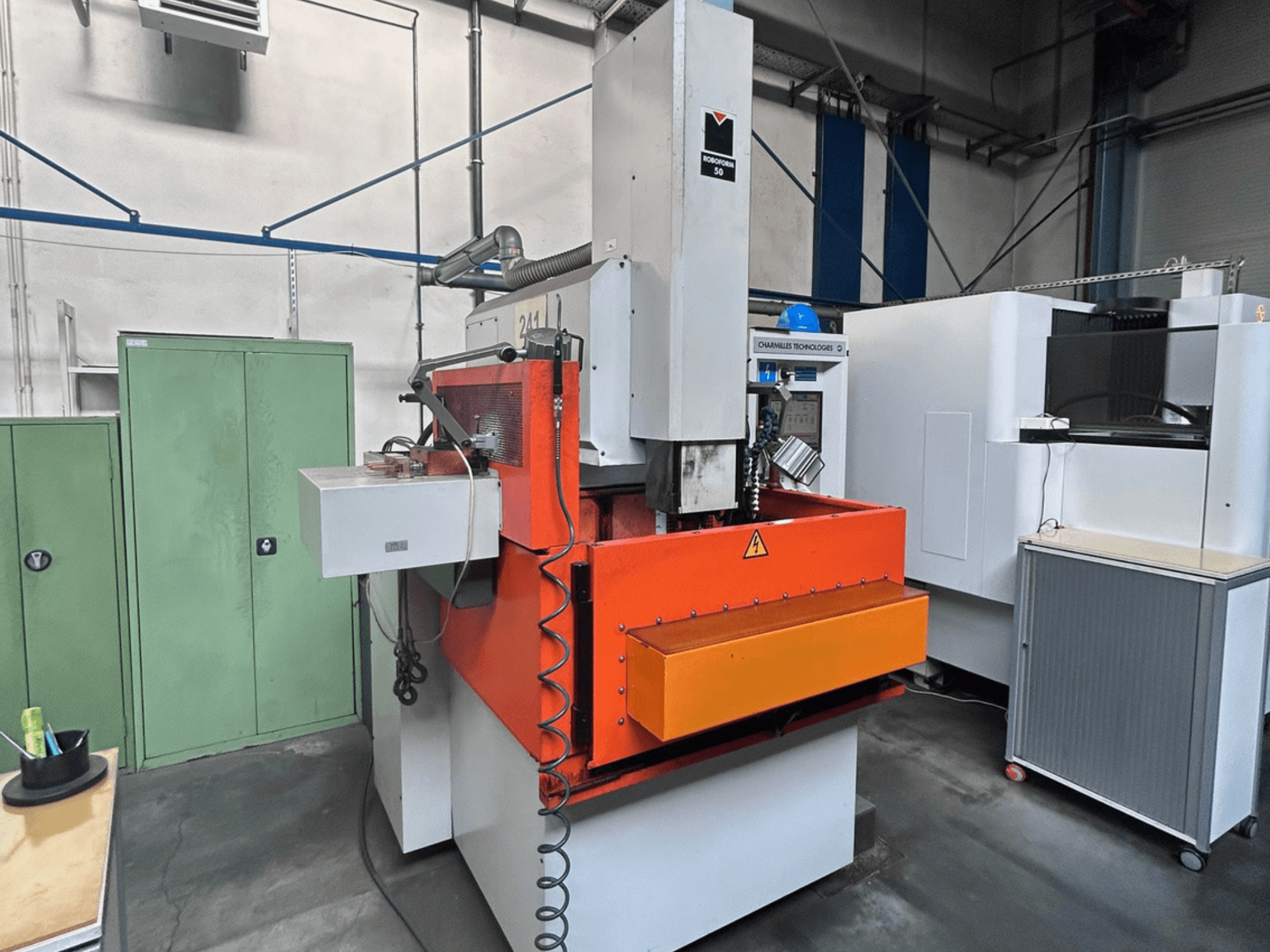 Front view of CHARMILLES ROBOFORM 50 Die-Sinking EDM Machine with orange panel, control interface, and surrounding equipment.