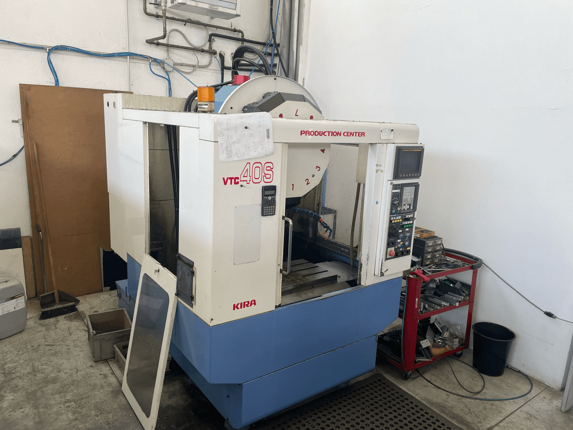 KIRA VTC 40S machining center in side view, featuring control panel, open door, and tools on a storage cart nearby.