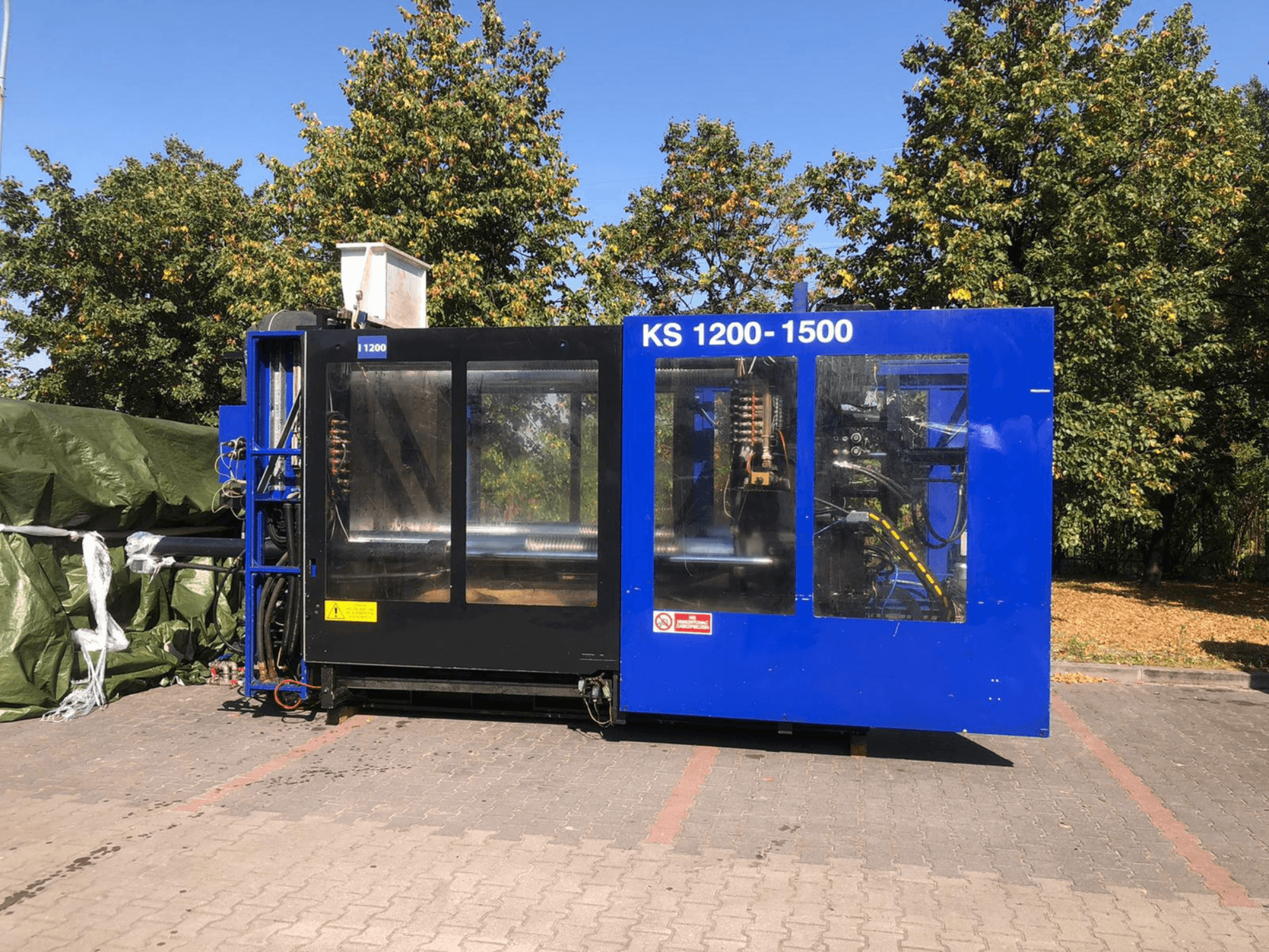 Hydraulic Injection Moulding Machine ITALTECH KS 1200 8300 ES, side view, showcasing controls and machinery details in a park setting.