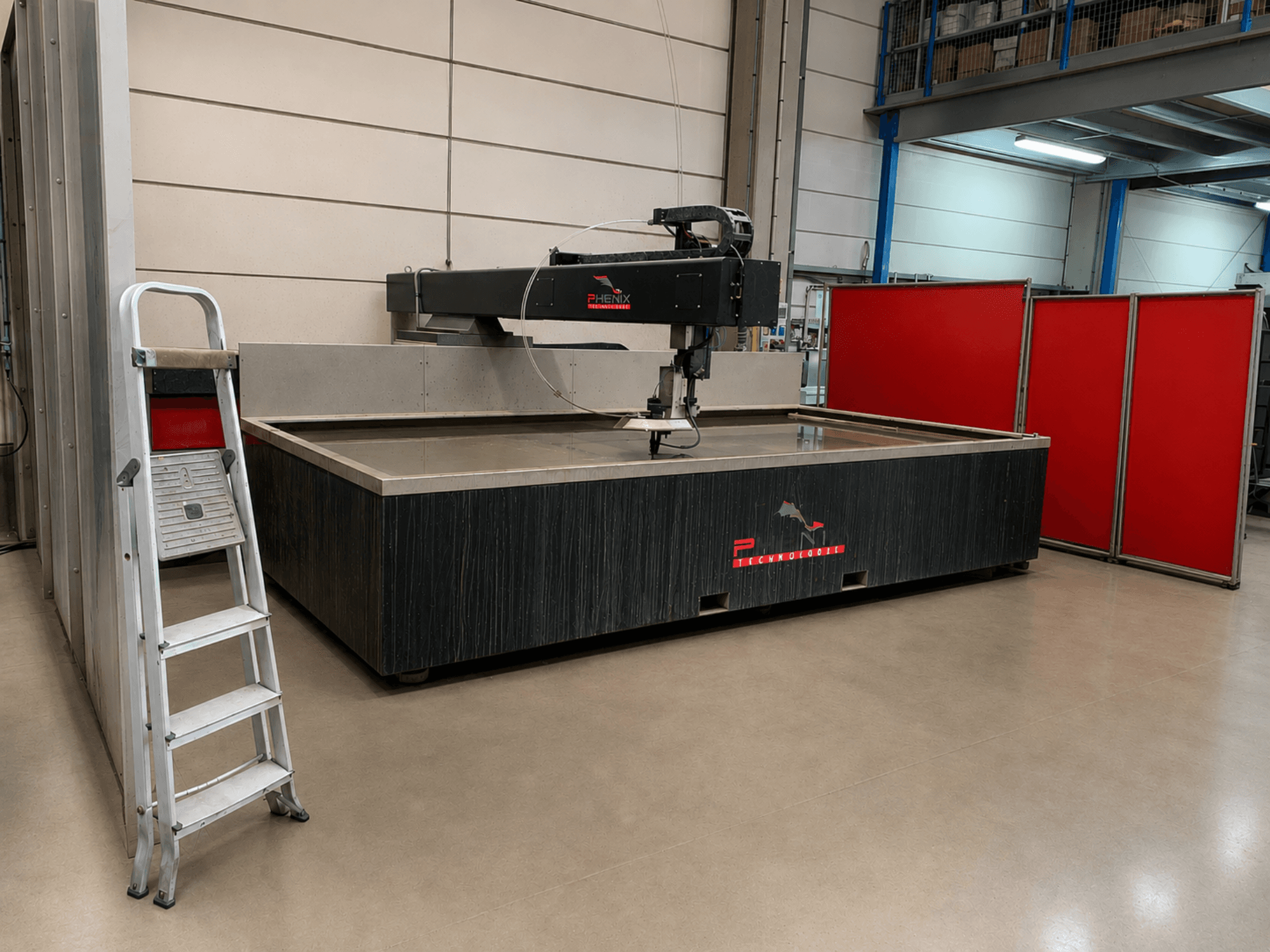 PHENIX TECHNOLOGIE MD-JET 2040 waterjet cutting machine in side view, with a silver ladder beside it and red partition panels.