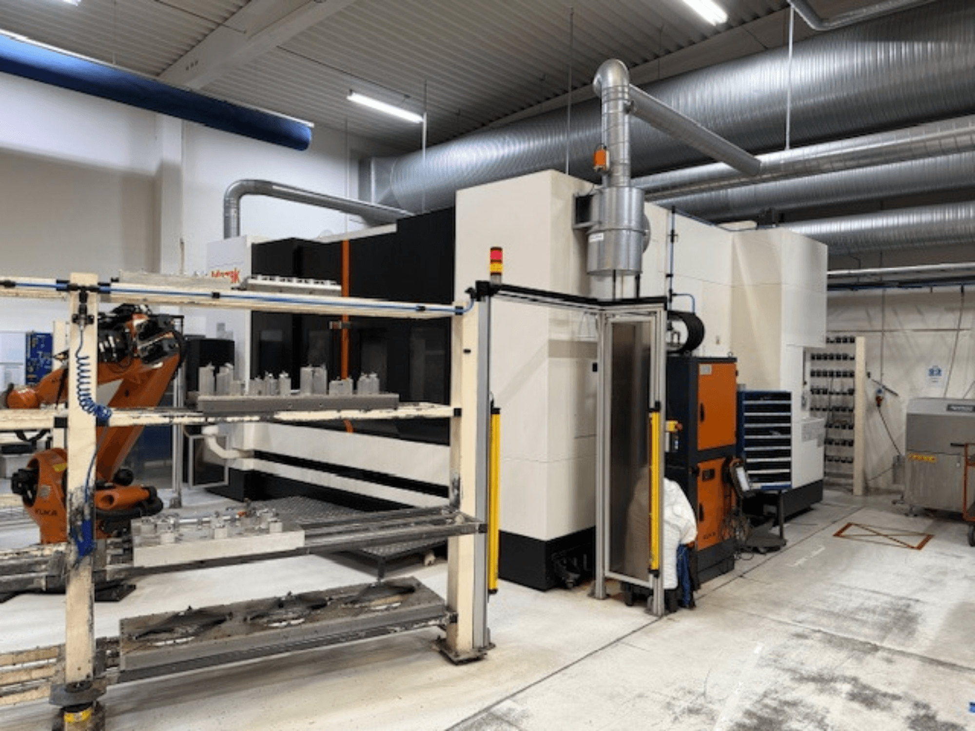 Industrial CNC machine with robotic arm and safety barriers, featuring a front view of the setup in an airy workspace.