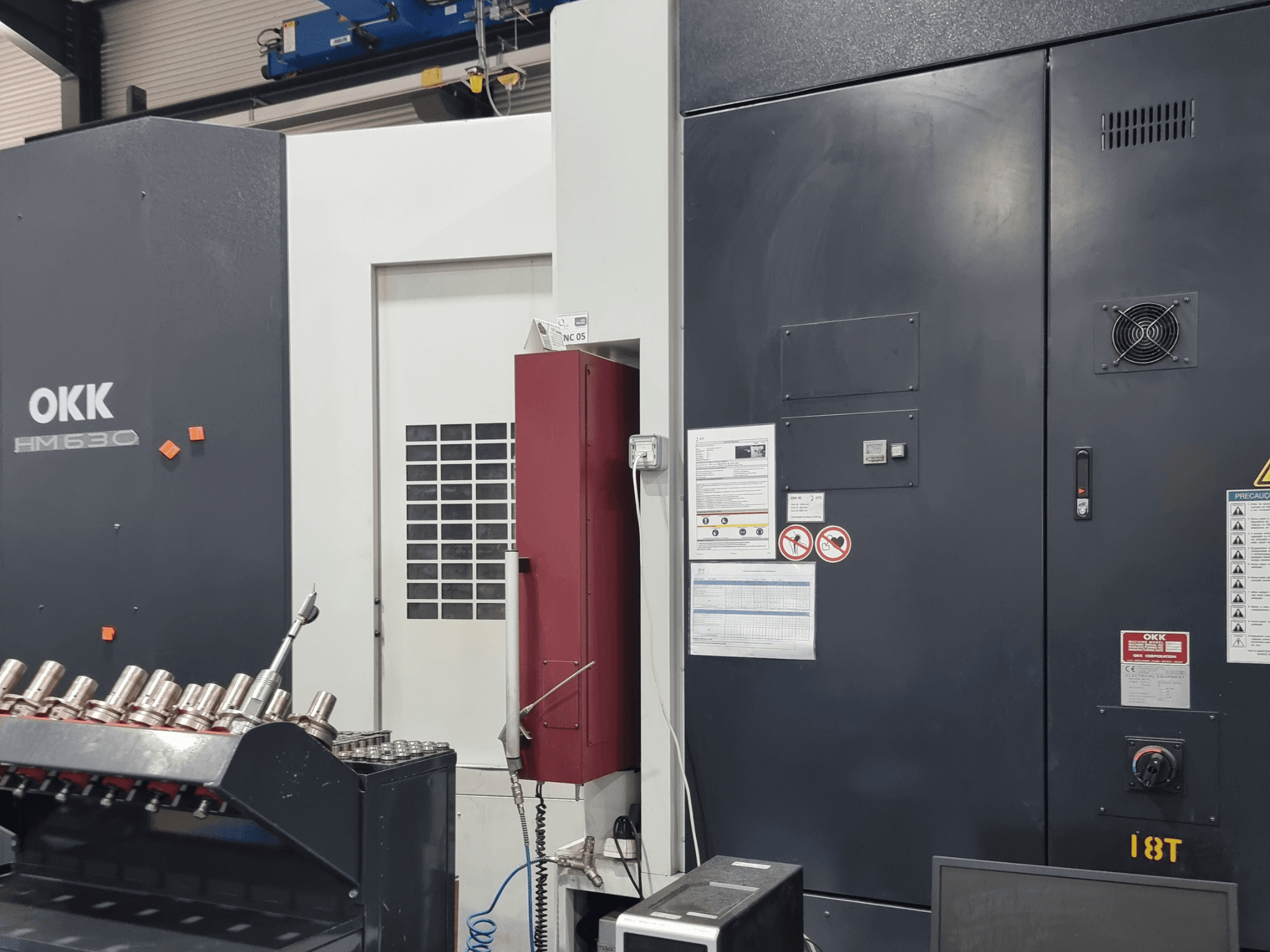 OKK HM630 horizontal machining centre, front view showing control panel, safety notices, and tool storage on the side.