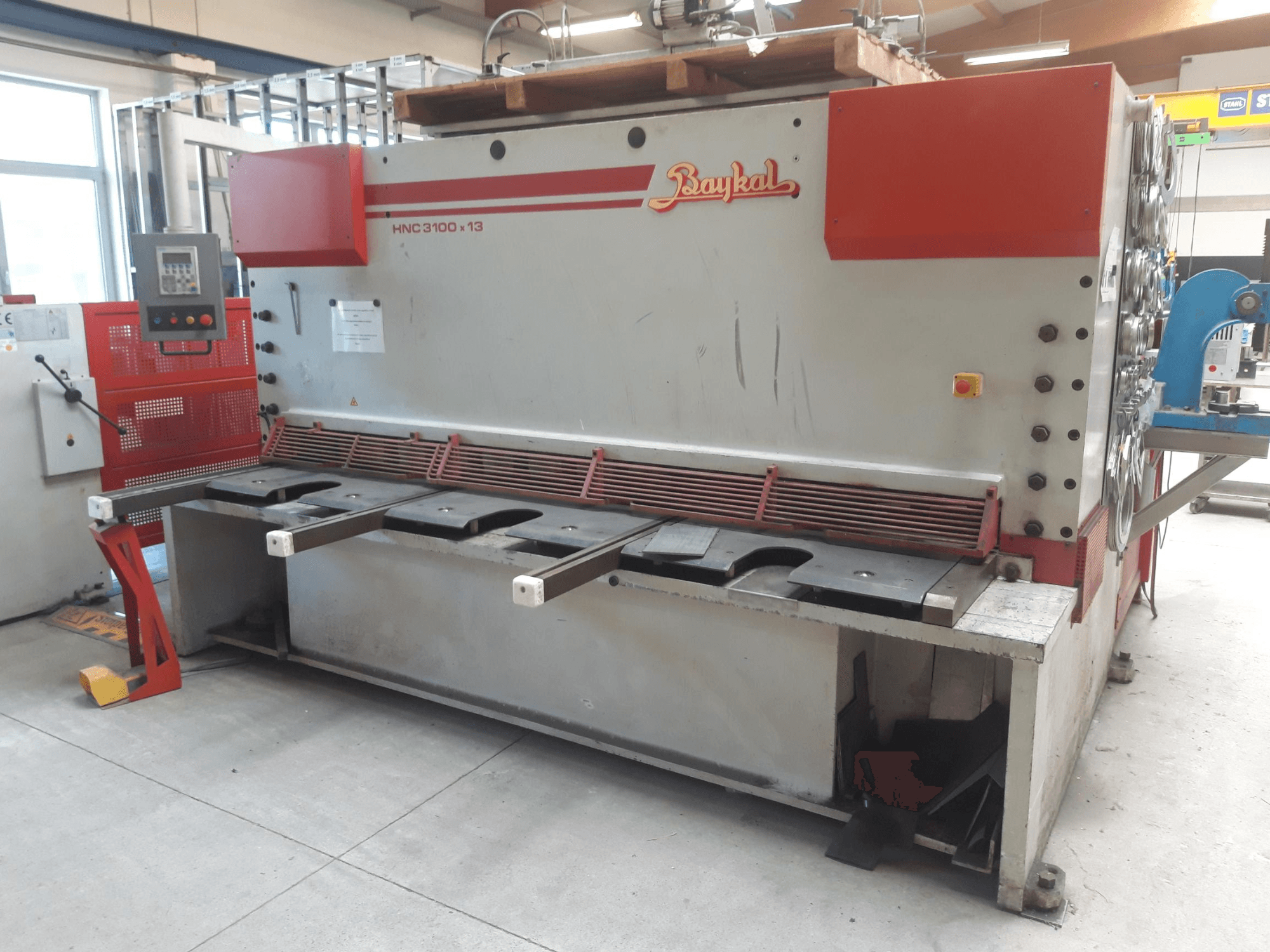 Baykal HNC 3100x13 CNC shearing machine front view, featuring a control panel, metal cutting area, and waste collection space.