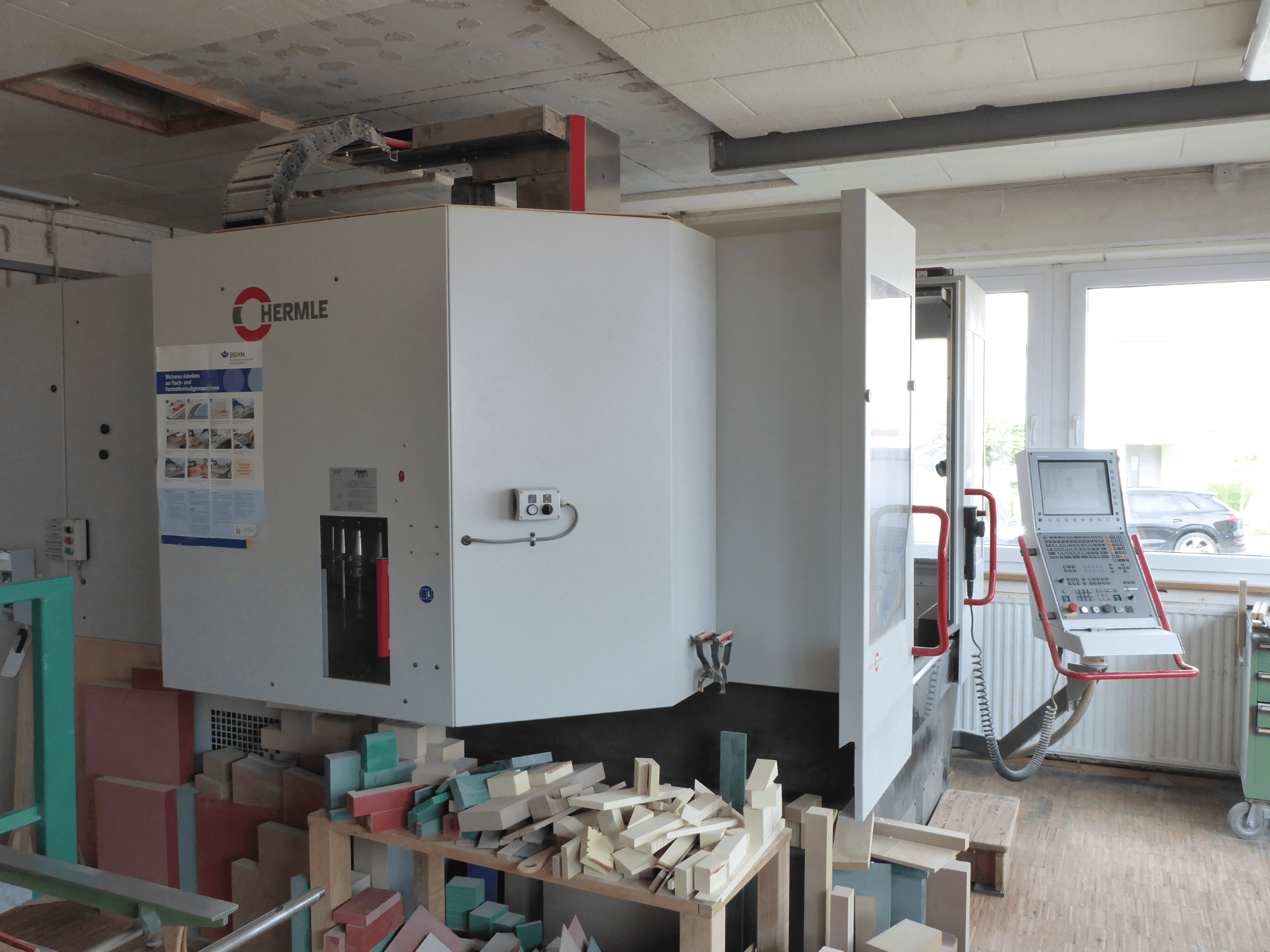 HERMLE C 1200 vertical machining centre in side view, displaying control panel and surrounding workpieces.