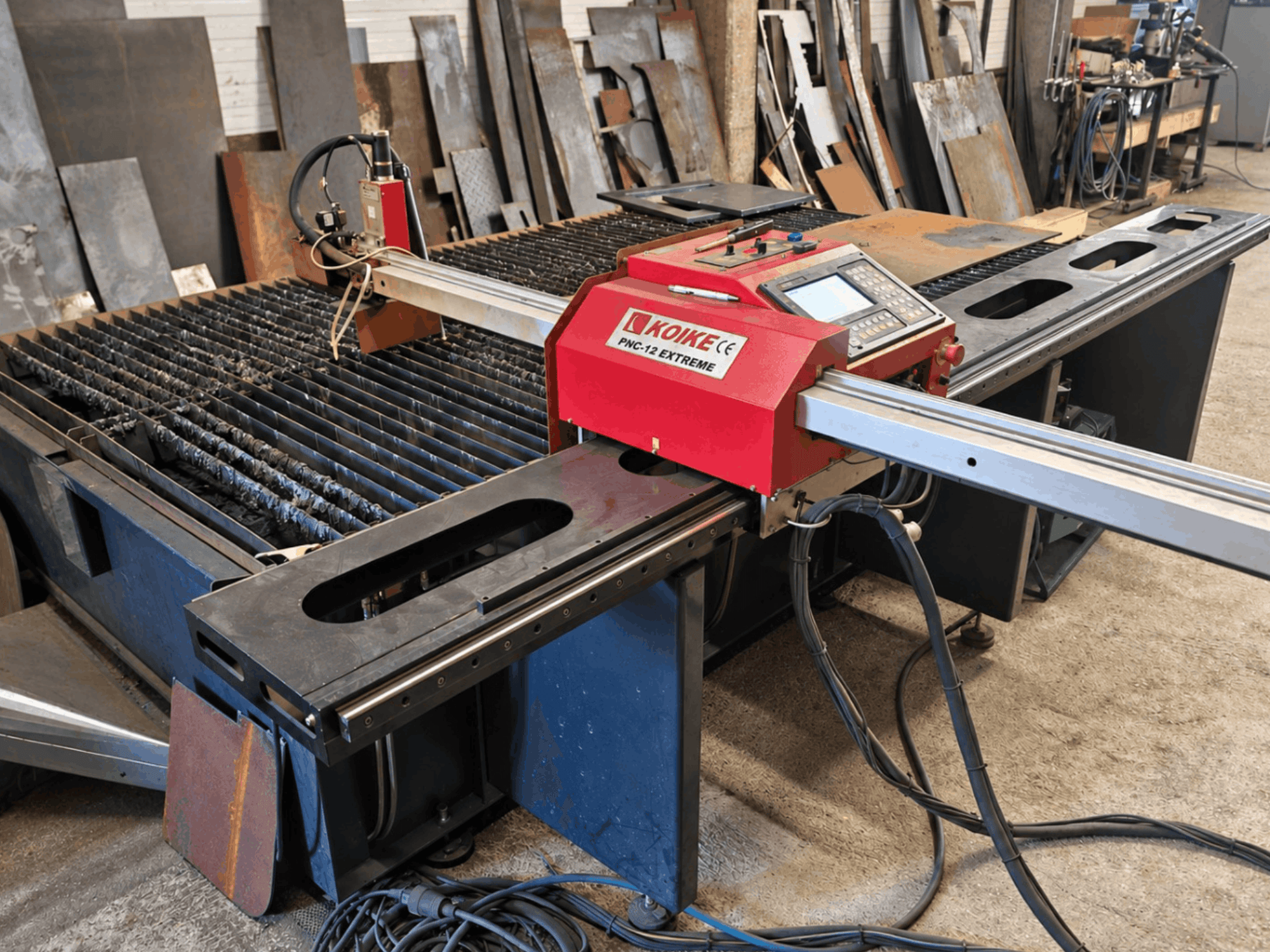 Front view of KOIKE PNC-12 Extreme plasma cutting machine with metal cutting table, control panel, and cables.