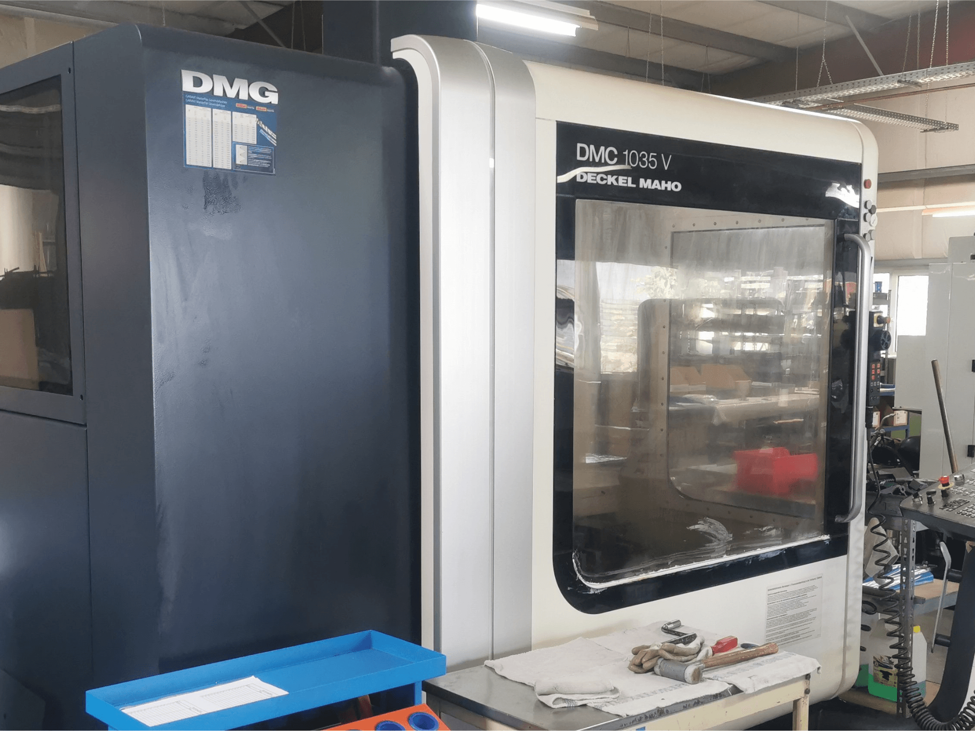 DMG DMC 1035 V milling machine in a workshop, front view with blue tool tray and gloves on the surface.
