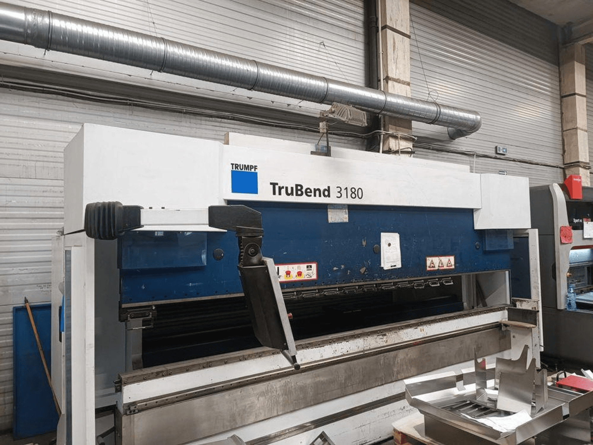 Trumpf TruBend 3180 bending machine in a workshop, side view showing control panel and metal pieces on the table.