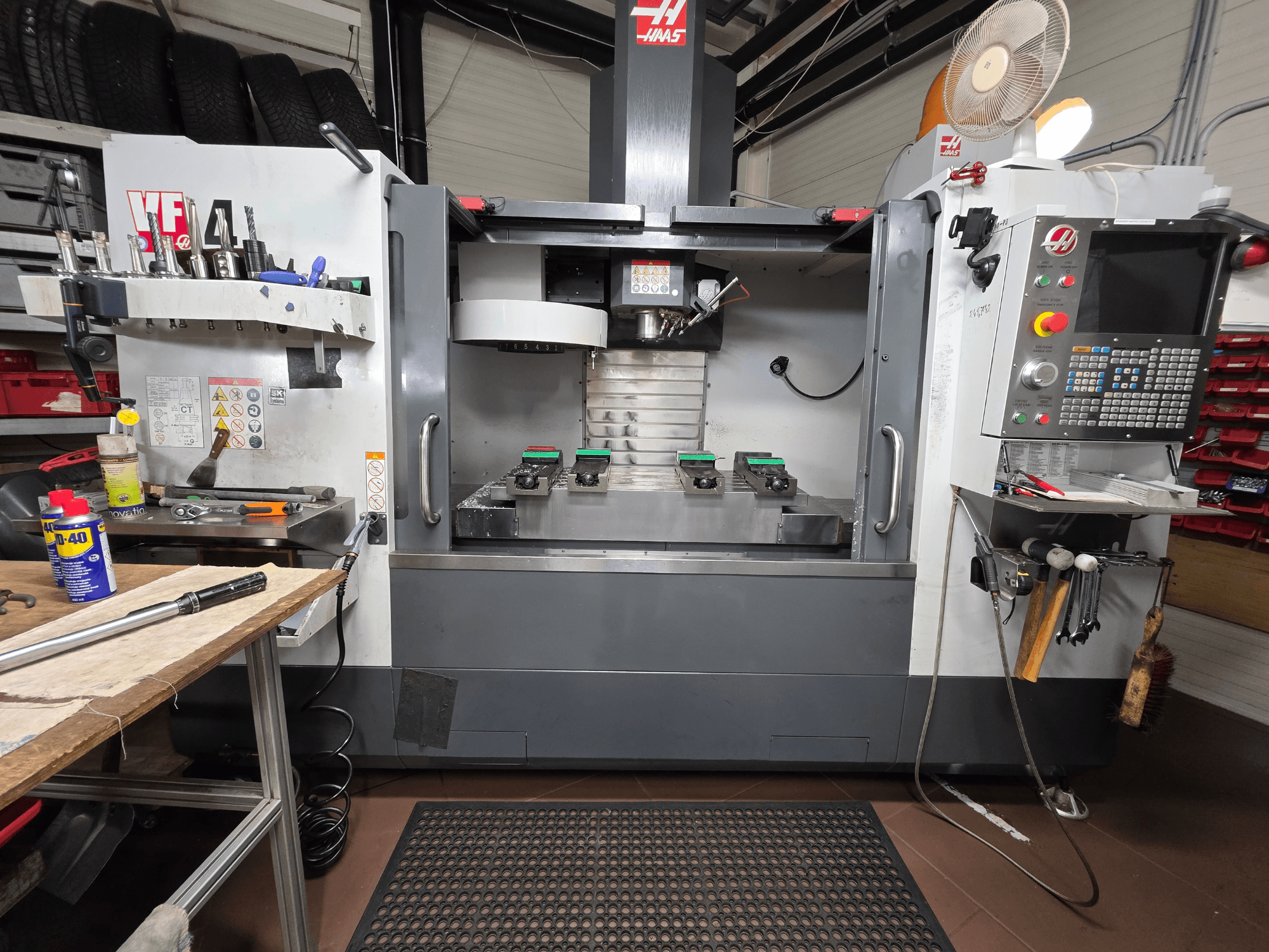 Haas VF-4 CNC mill front view in a workshop, featuring tools, a computer interface, and two workpieces on the table.