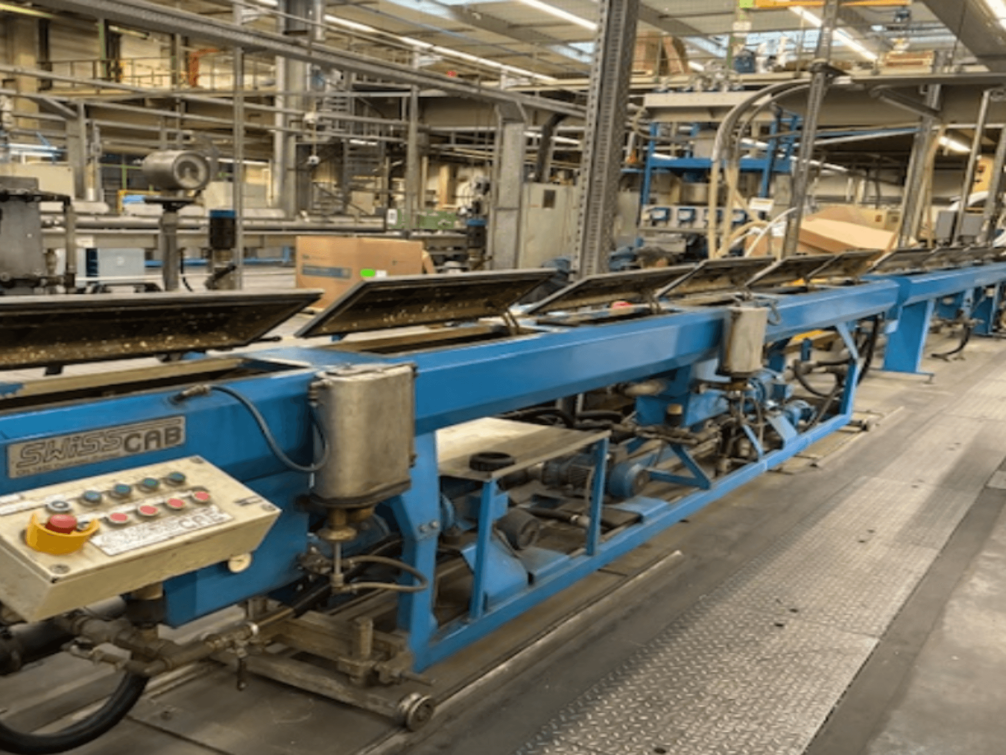 Blue SwissCab industrial machine in a factory setting, featuring operational buttons and a conveyor system, side view.
