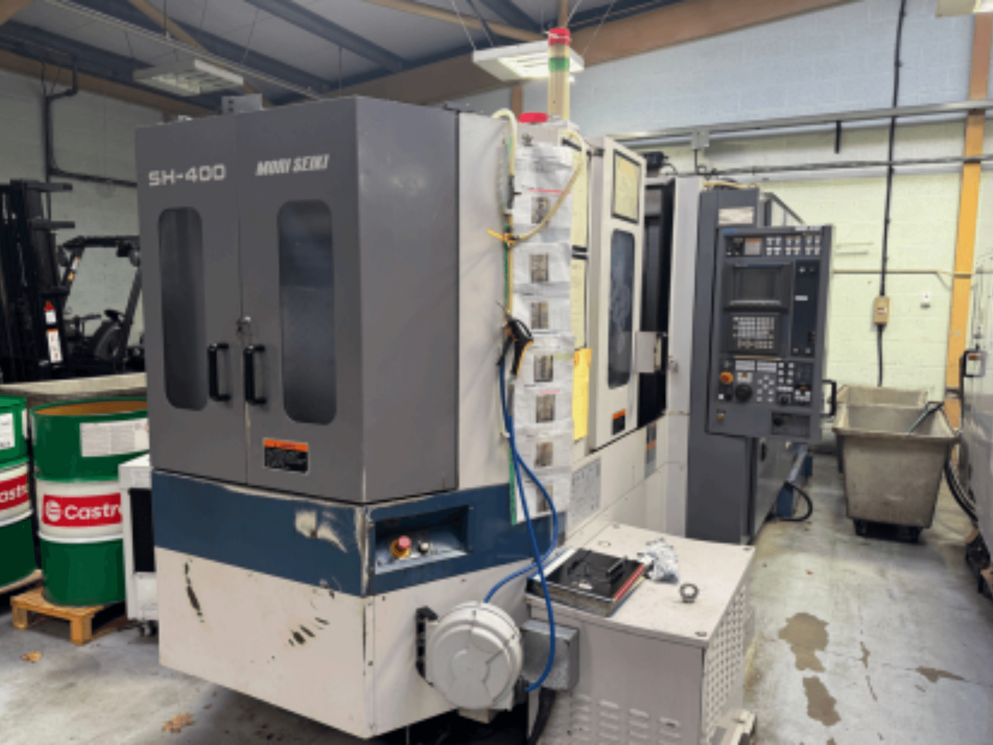 Moni Seiki SH-400 CNC machine, side view showing control panel, doors, and surrounding industrial environment.