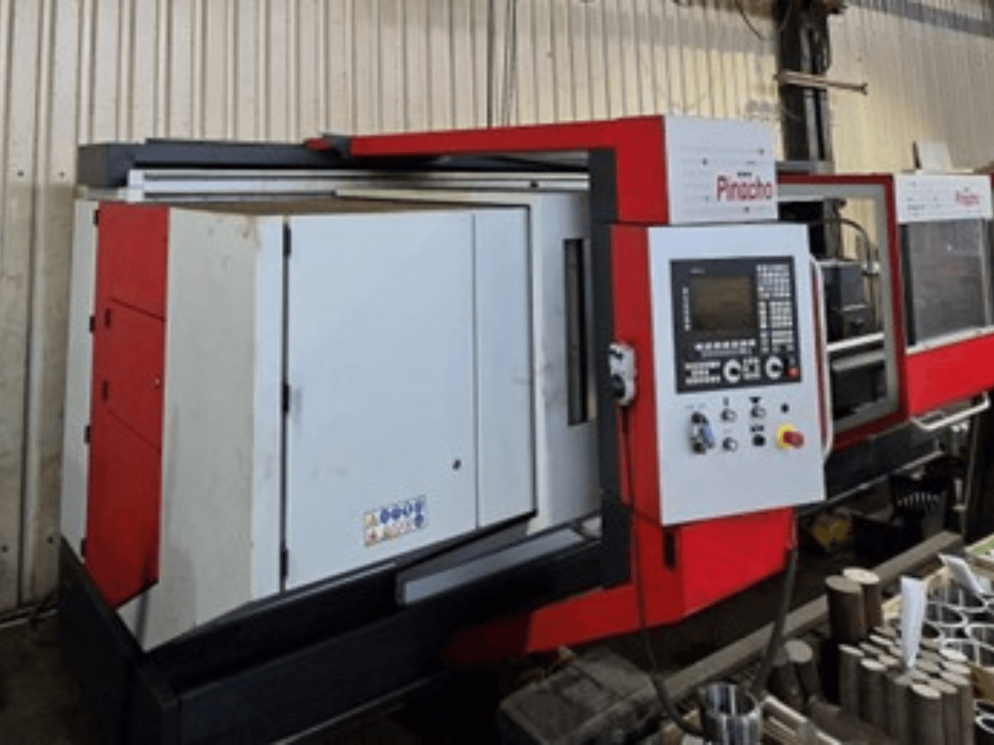 Pinacho CNC machine in red and white, side view, with control panel and materials on the floor, showing operational setup.