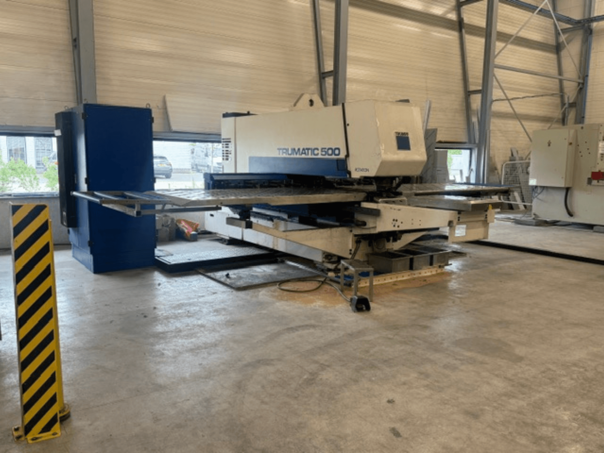 CNC punching machine TRUMPF Trumatic 500 in a workshop, side view showing machinery and safety post with yellow stripes.