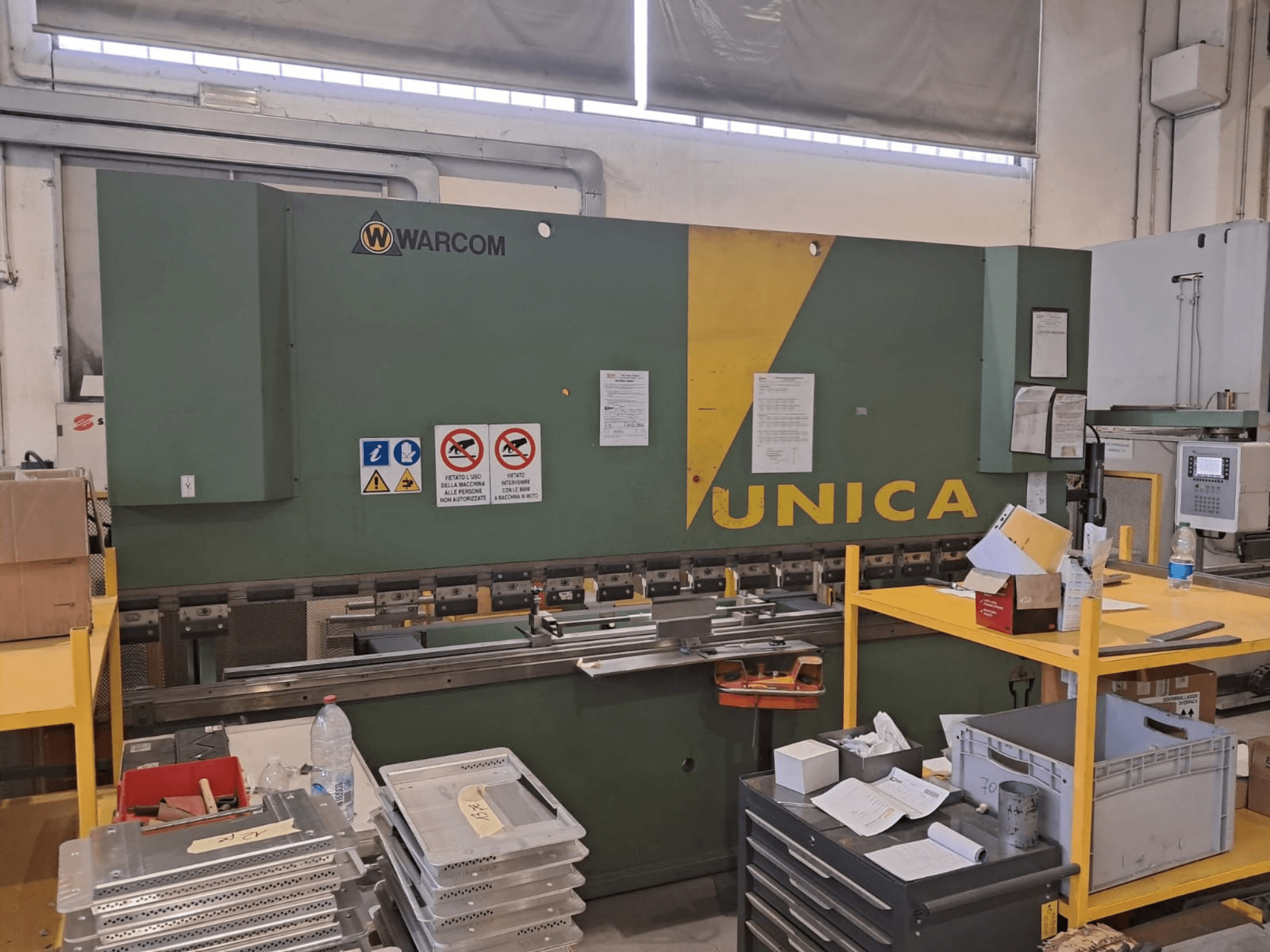 Hydraulic press Warcom UNICA 100-40, front view, green body with yellow accents, safety signs visible, tools and materials on table.