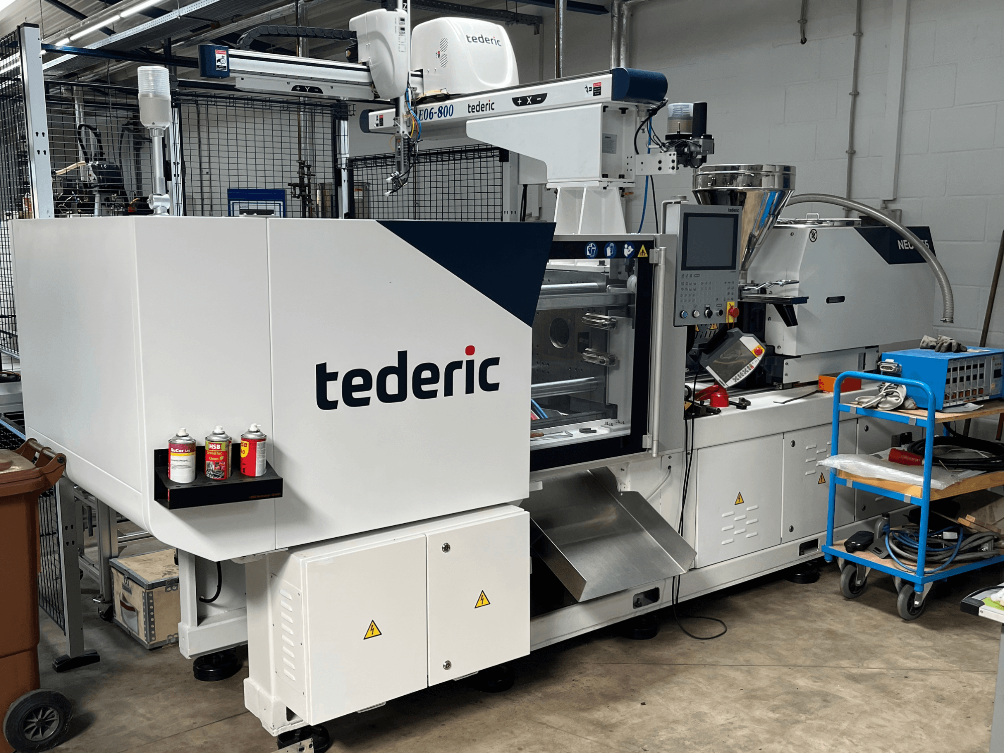 Hydraulic Injection Moulding Machine TEDERIC NEO.E55/e110h in a workshop, side view with control panel and adjacent tools.