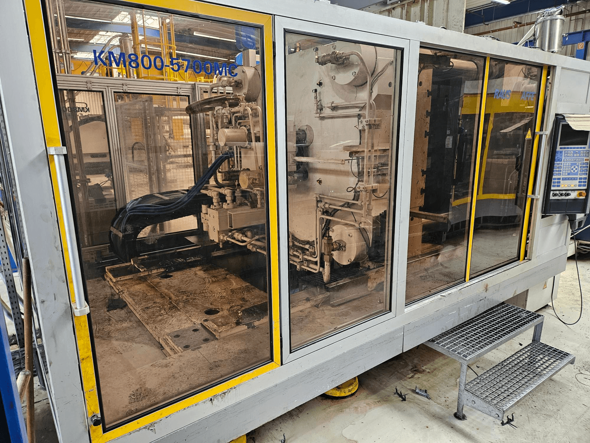 Hydraulic injection moulding machine Krauss Maffei KM800-5700 MC, front view showing components through glass panels.