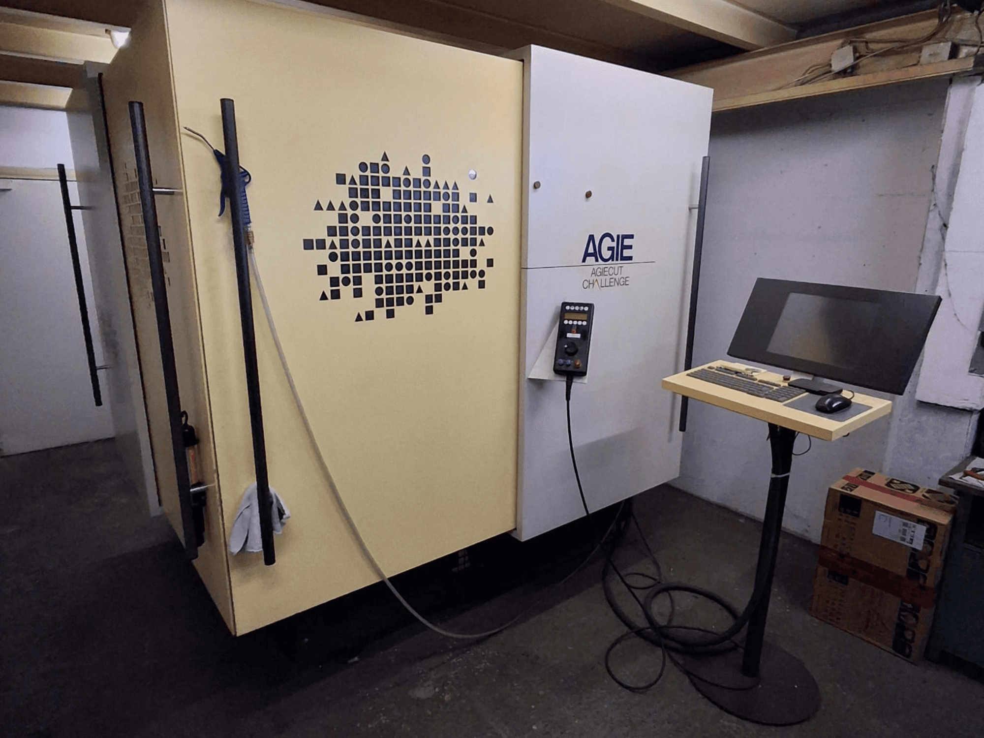AGIE Agiecut Challenge 2 wire EDM machine in a workshop, featuring control panel and monitor on a stand, front view.