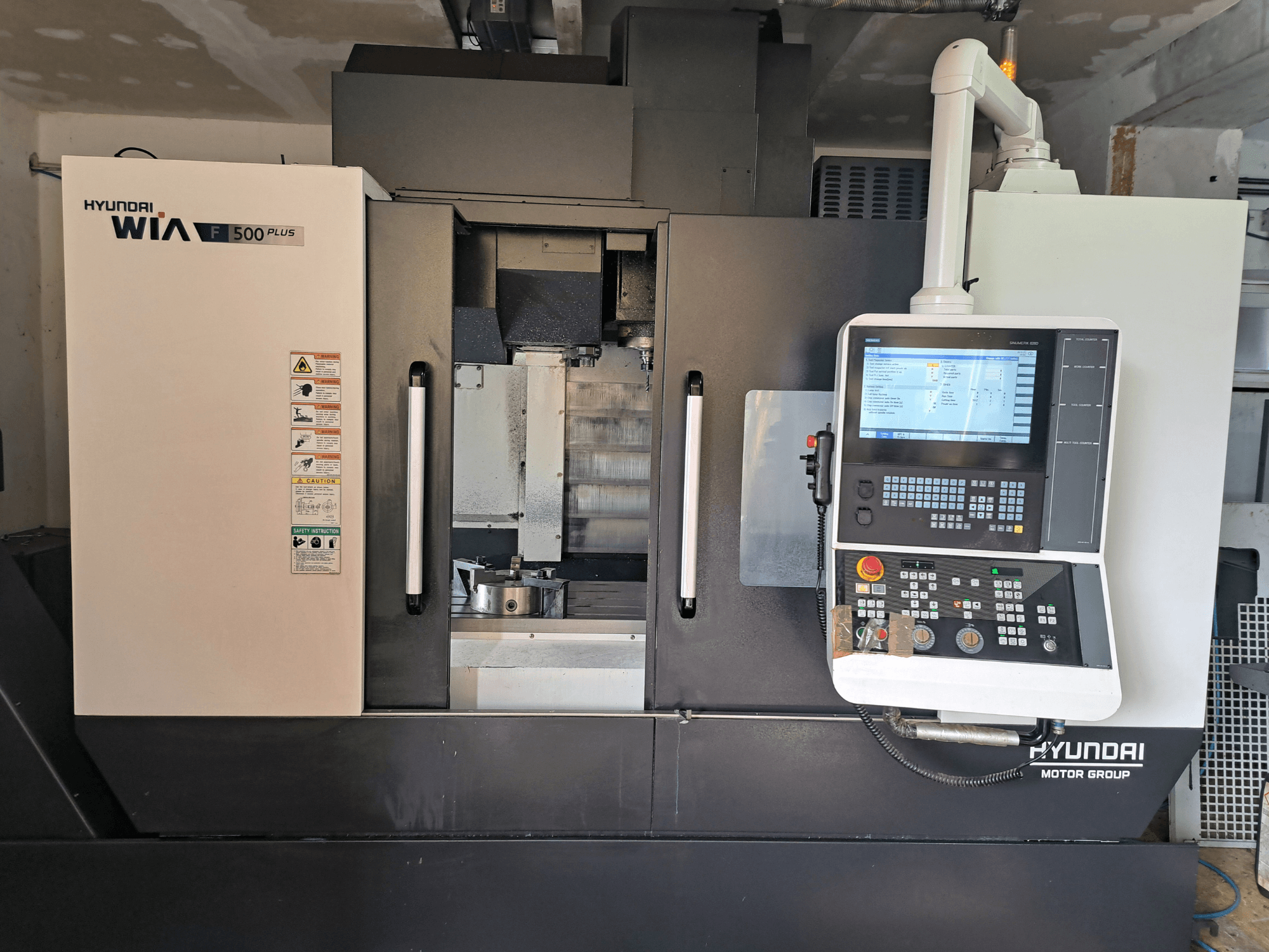 Hyundai WIA F500 Plus CNC machine in front view, featuring a digital control panel and safety labels.