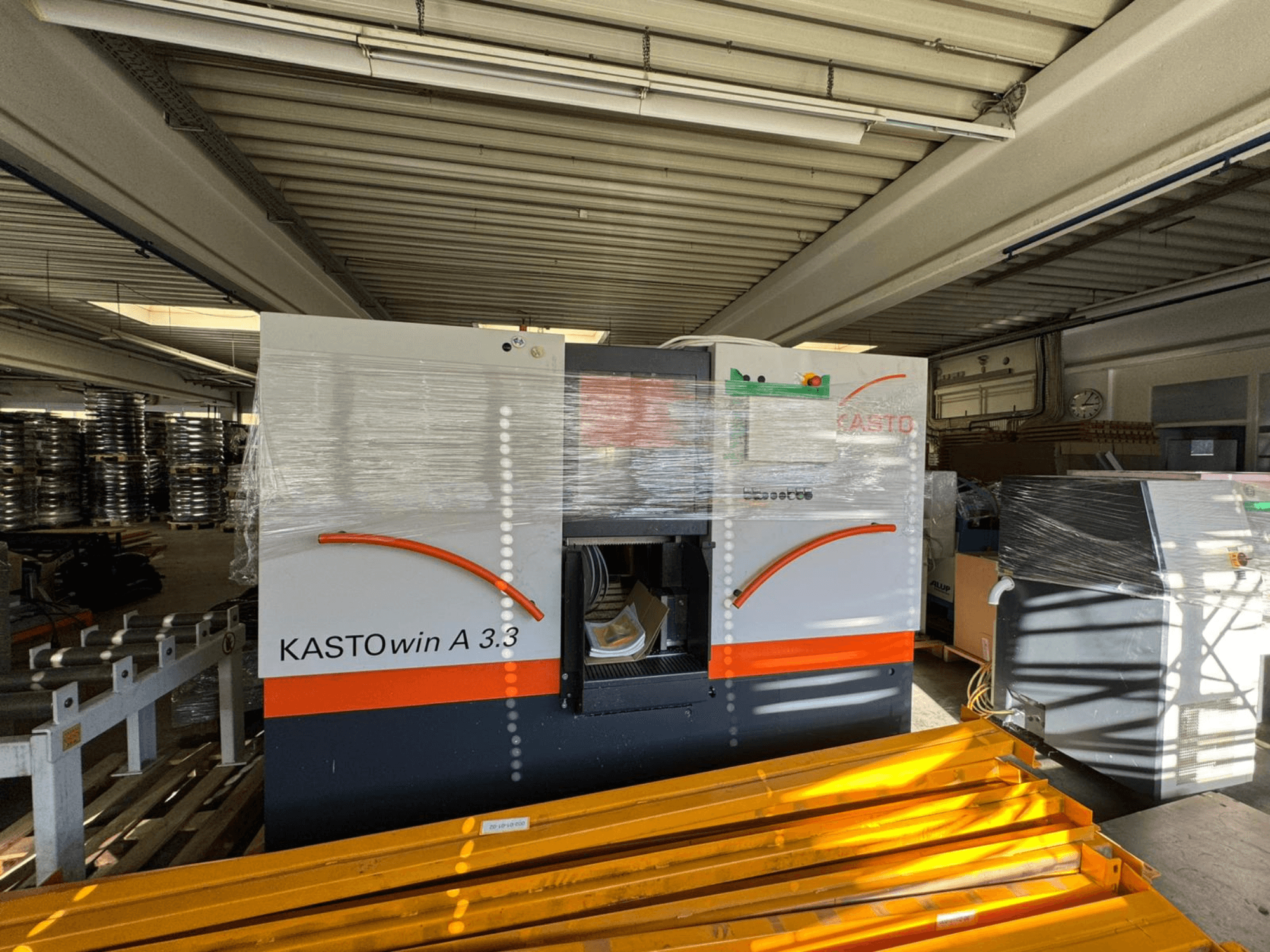 KASTO win A 3.3 metal band saw in a front view, wrapped for protection, with operational controls and surrounding equipment visible.
