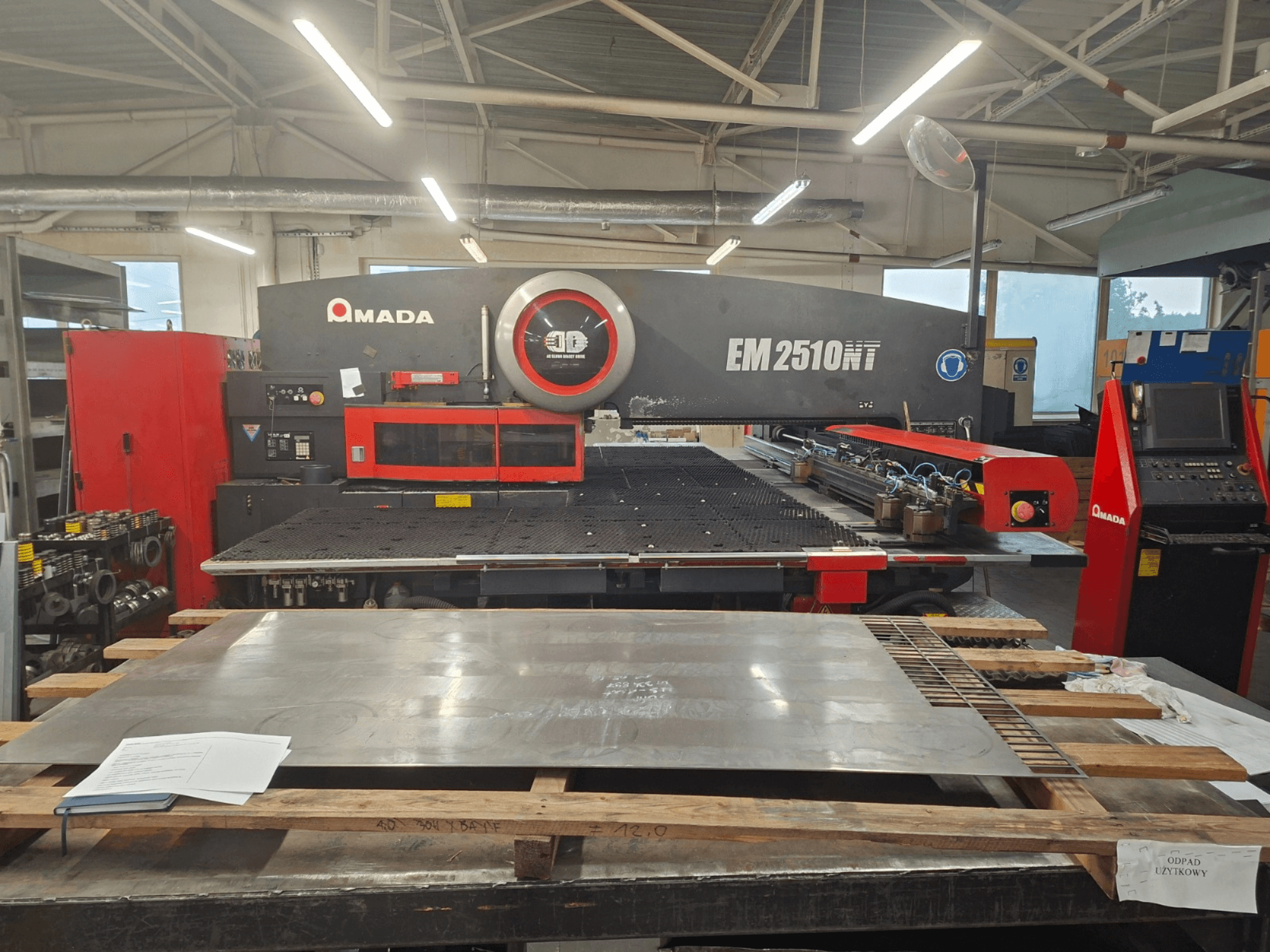 Front view of AMADA EM 2510NT turret punch press, with metal sheet and control panel visible in a workshop setting.