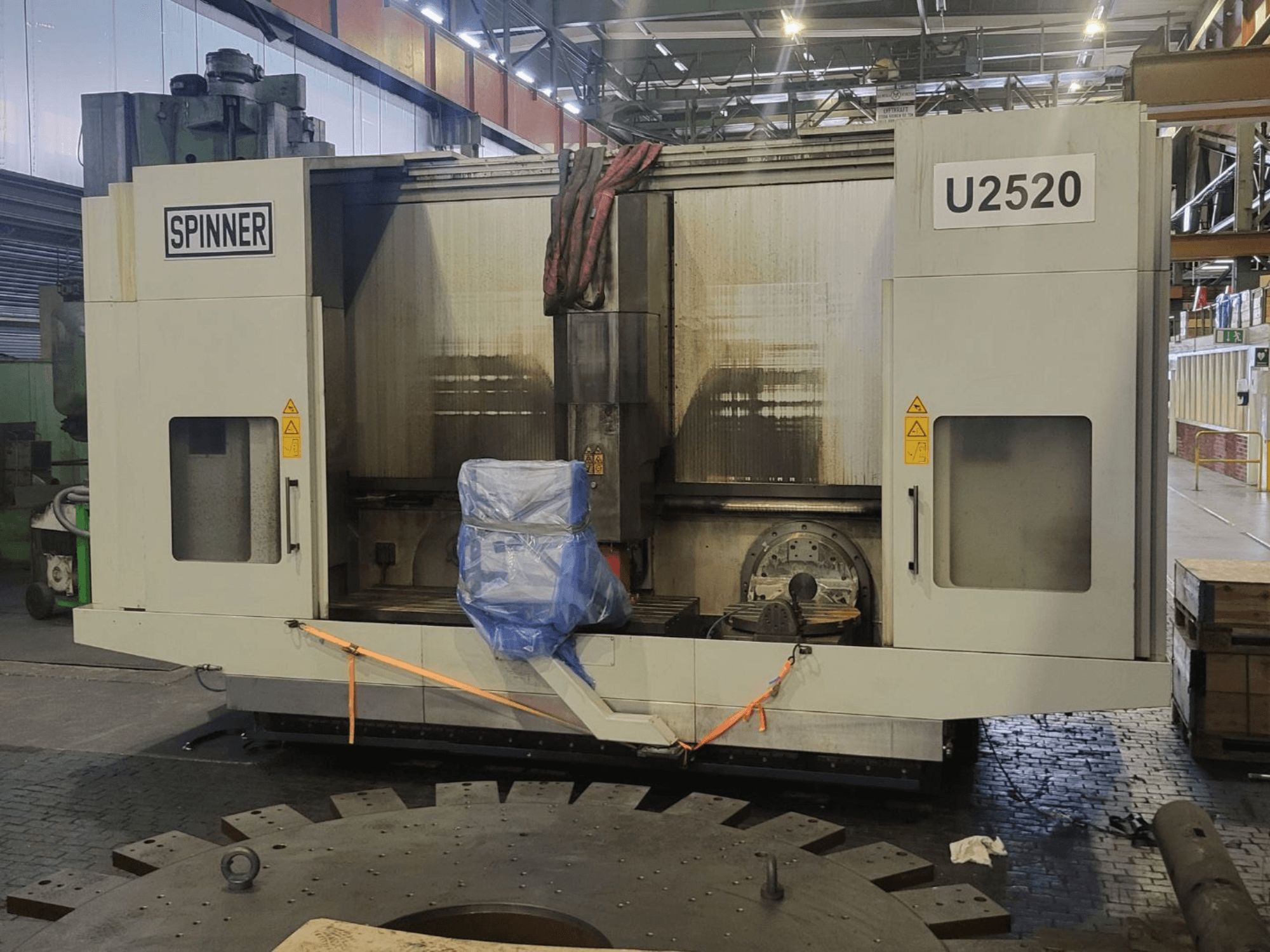SPINNER U5-2520 vertical machining centre shown from front view, featuring a covered table and safety labels.